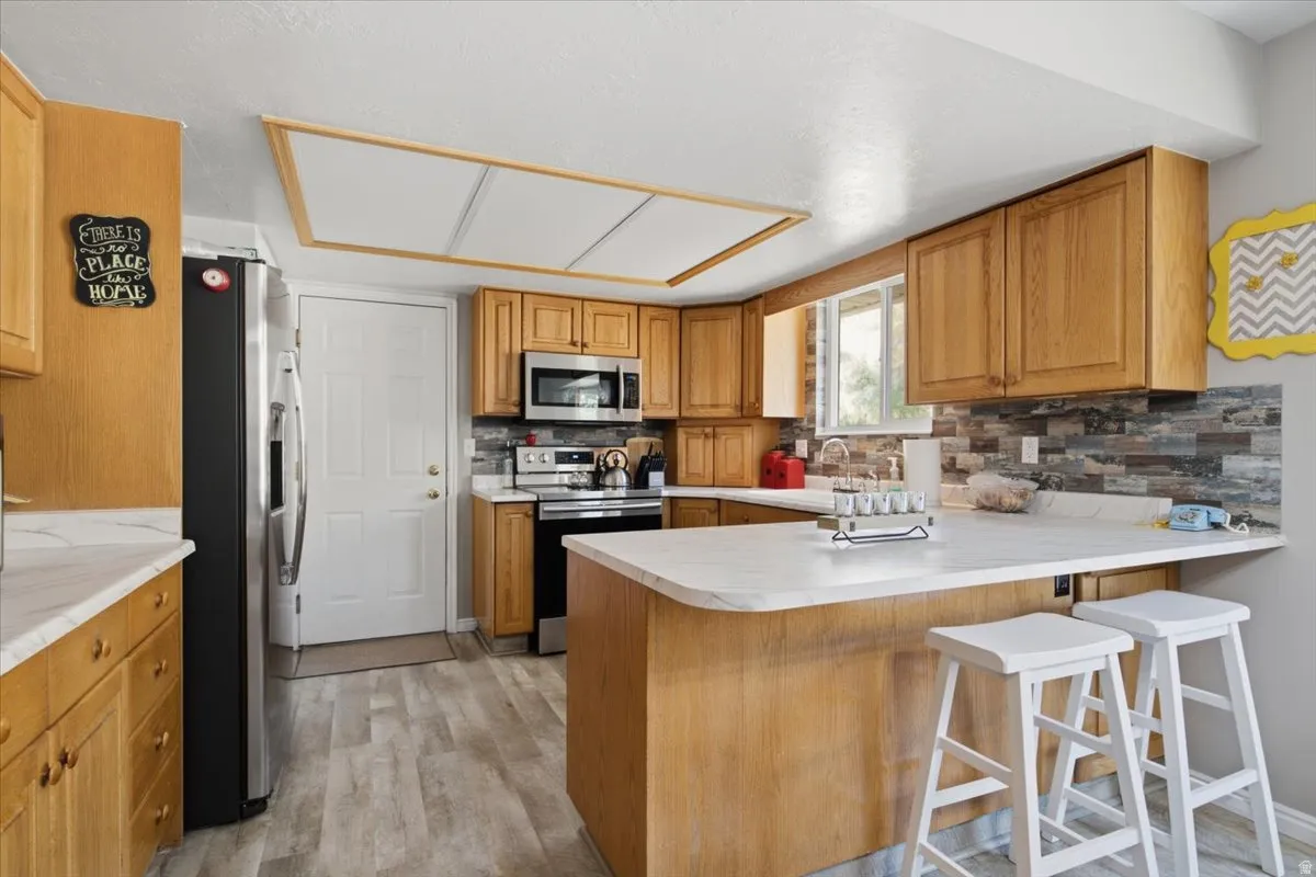 Kitchen featuring wood cabinetry, light-toned countertops, a stacked stone-look backsplash, and wood-finish flooring