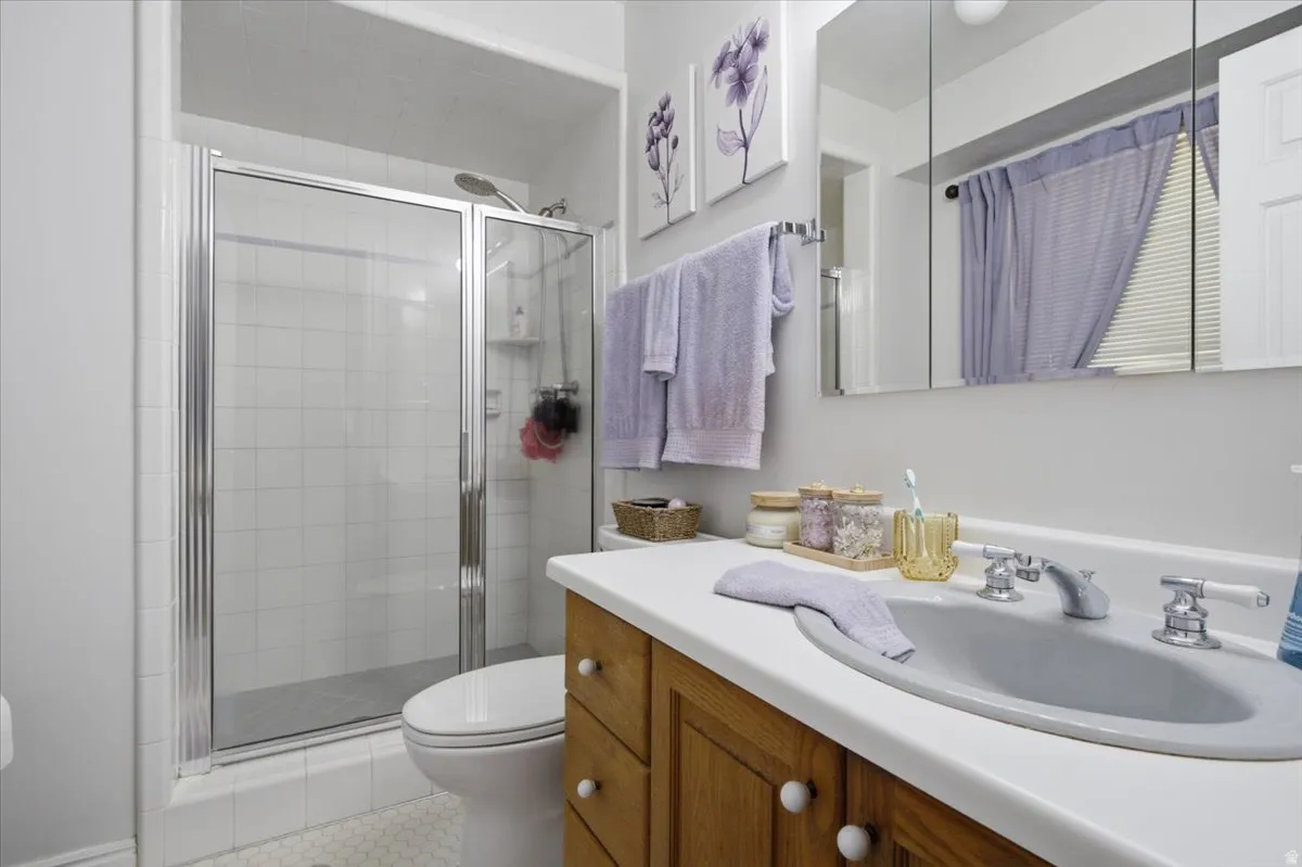 Main En-Suite Bathroom featuring a glass-enclosed shower with white tiled walls, a wood-finish vanity with a white countertop and integrated sink, and hexagon tile flooring