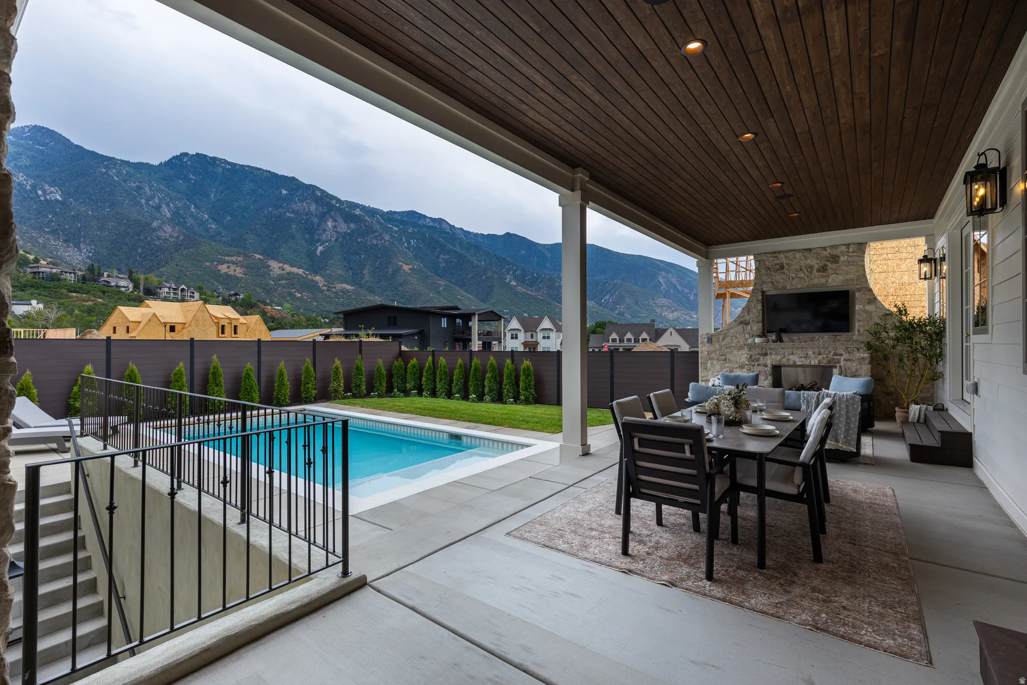 Expansive covered patio featuring a wood-finish ceiling with recessed lighting, an outdoor fireplace with stone surround, and an adjacent swimming pool