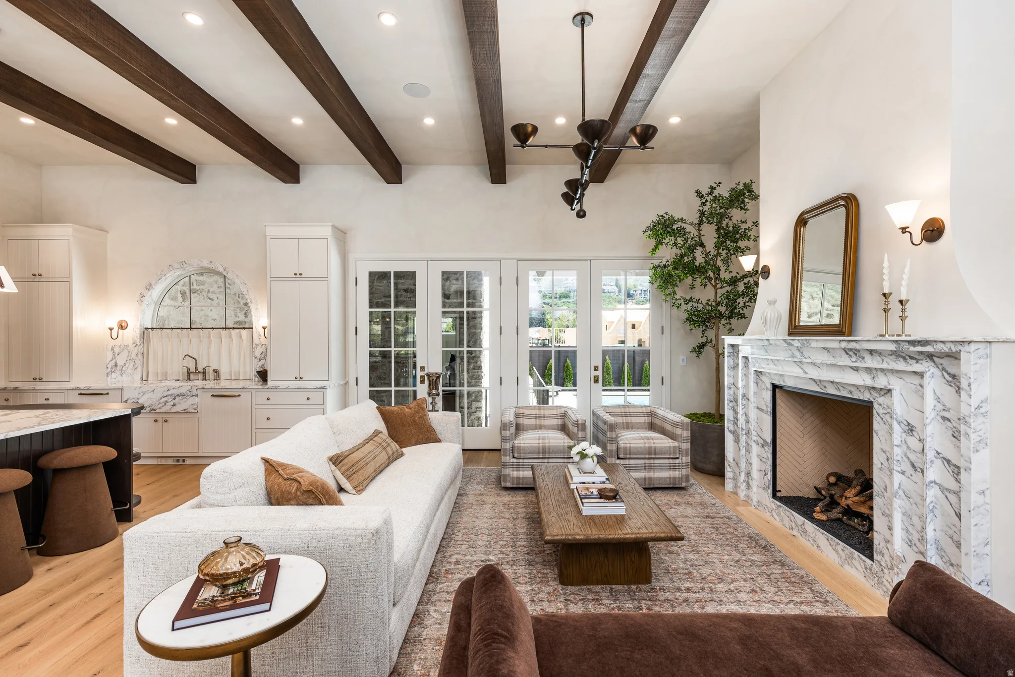 Vaulted ceiling with exposed wood beams, marble fireplace with a herringbone interior, light wood-finish flooring, white cabinetry, and French doors