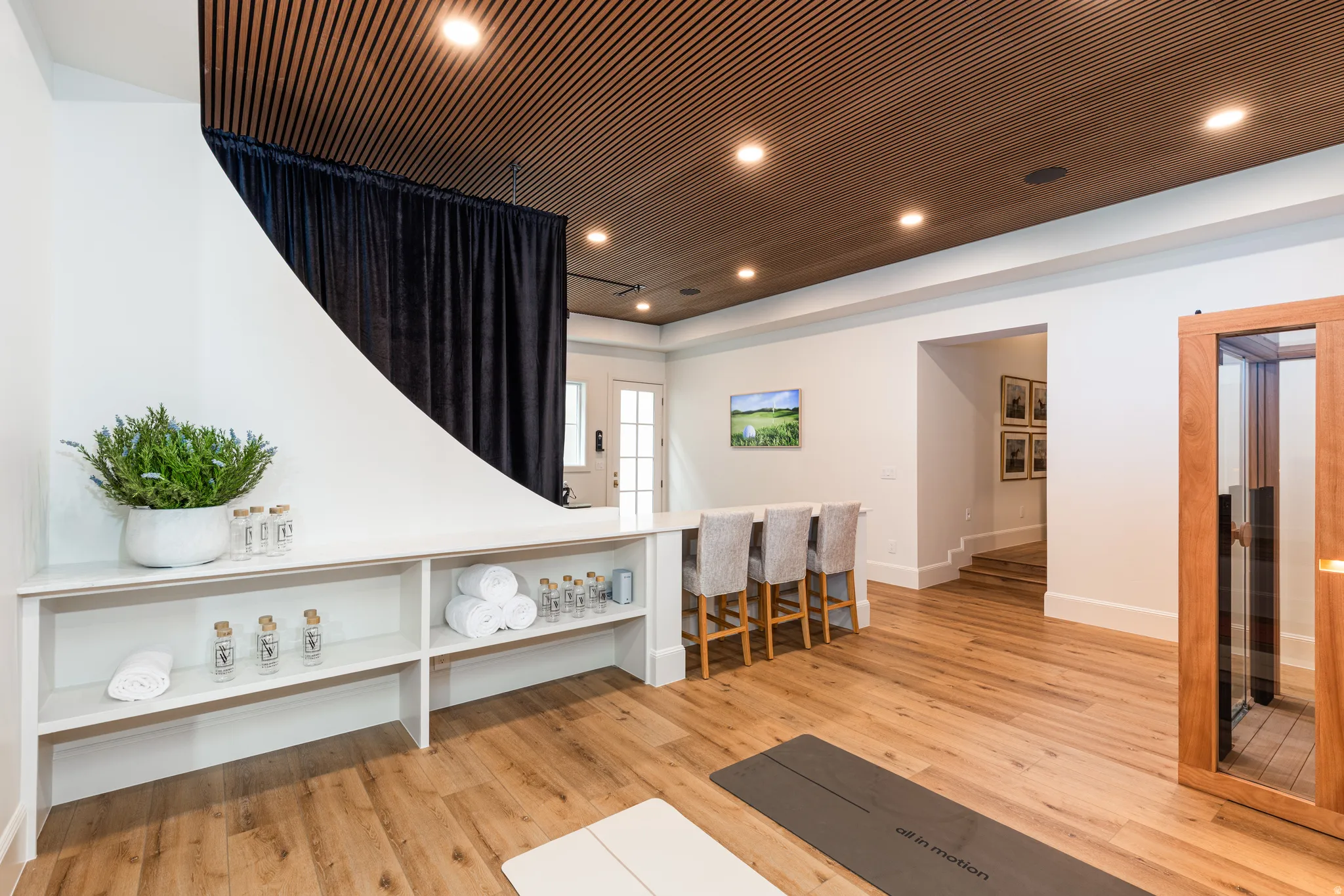 Spacious room featuring wood-finish flooring, a contemporary wooden slatted ceiling with recessed lighting, and a built-in white shelving unit