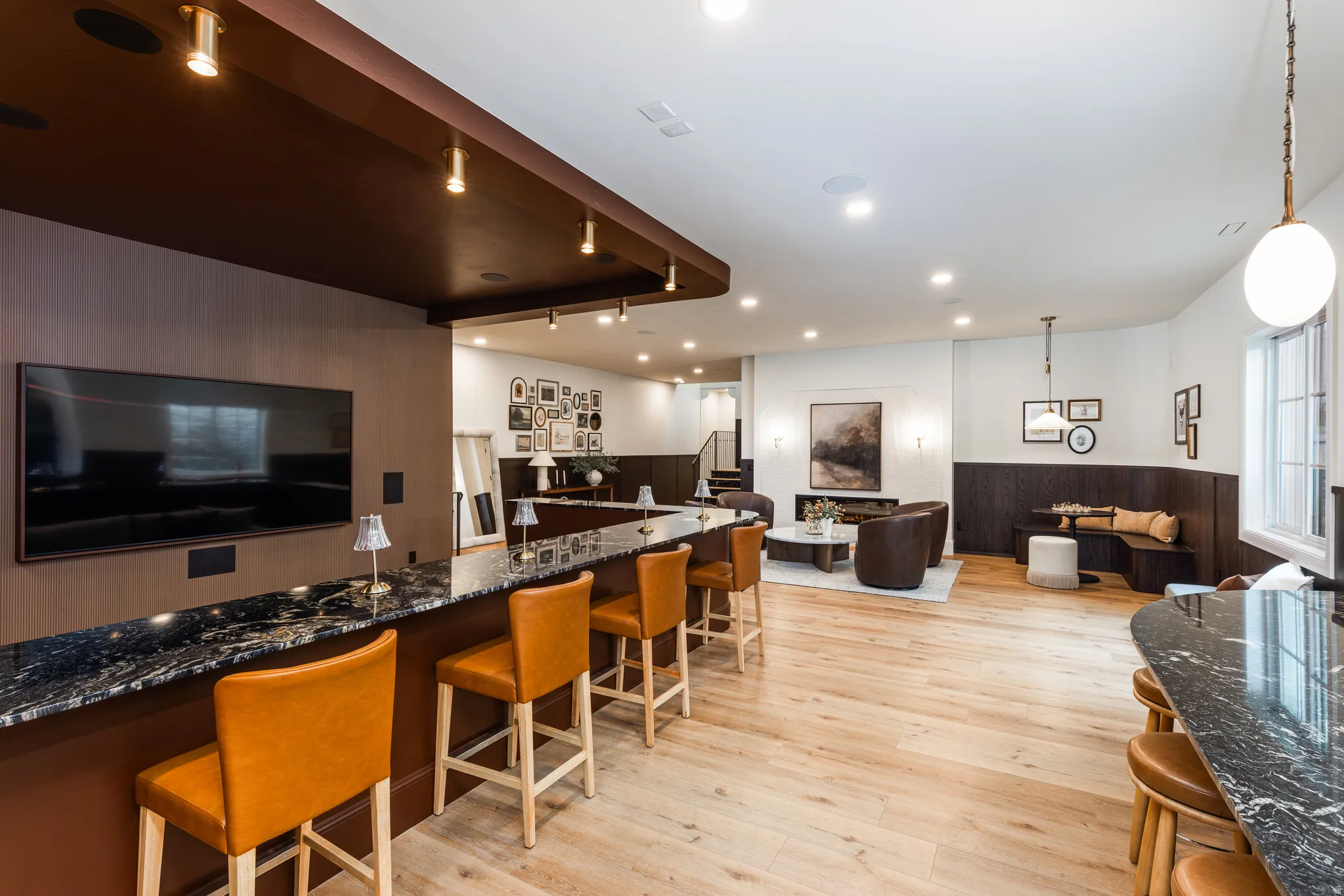 Expansive entertainment space featuring light wood-finish flooring, a built-in bar with dark stone countertop, recessed lighting, and a built-in banquette seating area