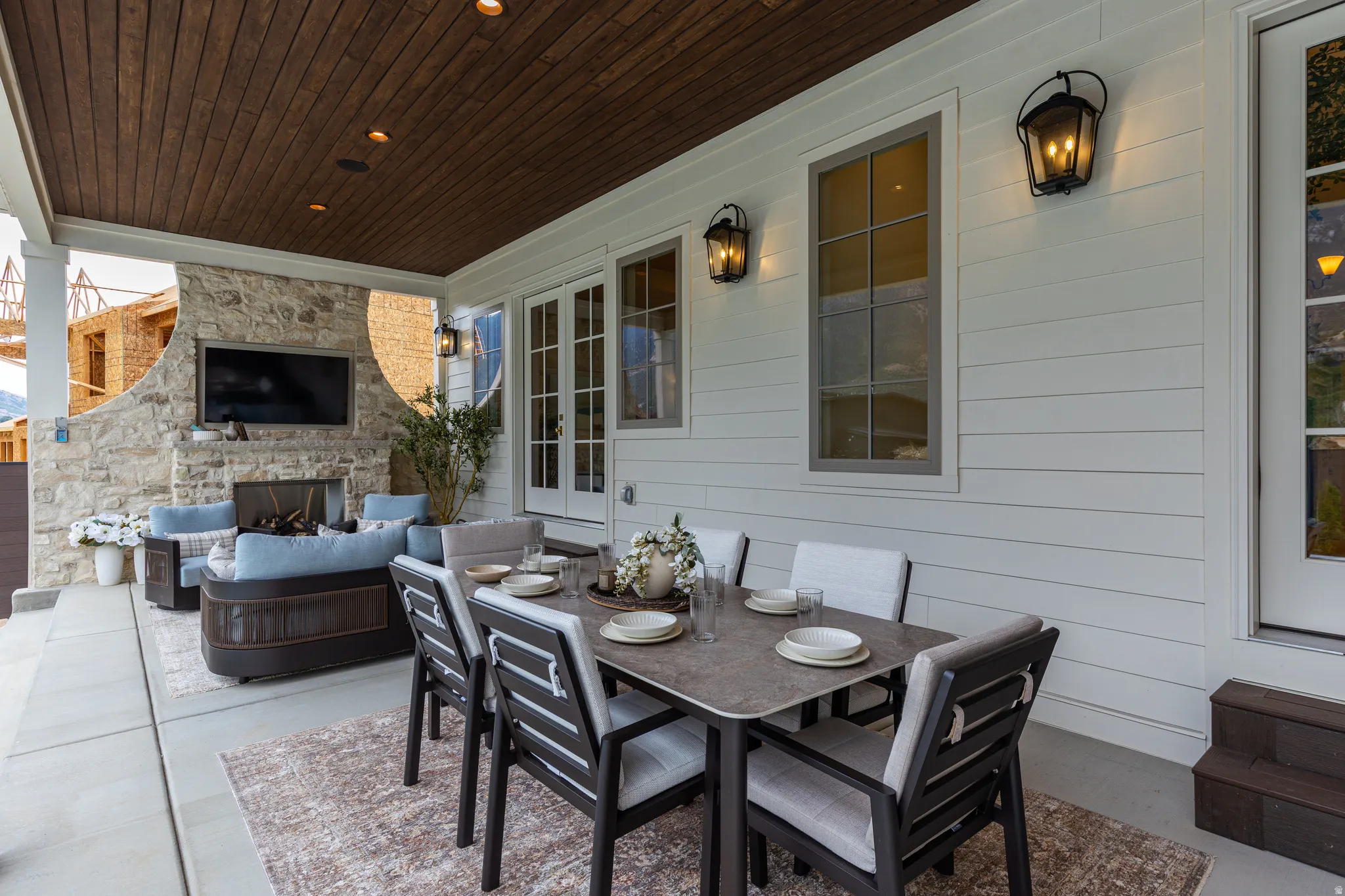 Covered outdoor patio featuring a wood-panel ceiling with recessed lighting, a stone-clad fireplace, and white horizontal siding