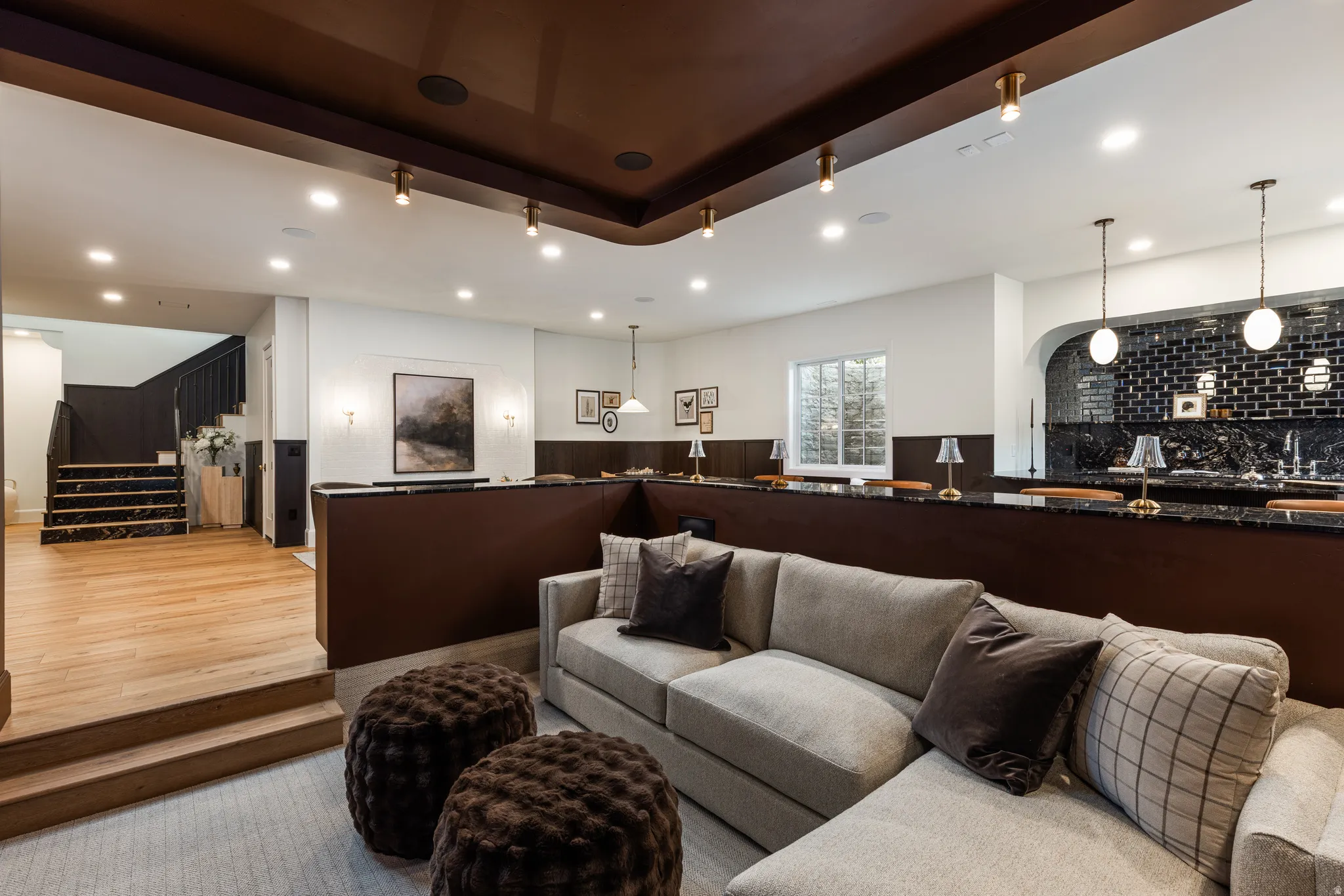 Multi-level entertainment space featuring a dedicated wet bar with black subway tile, a recessed archway, and dual pendant lighting