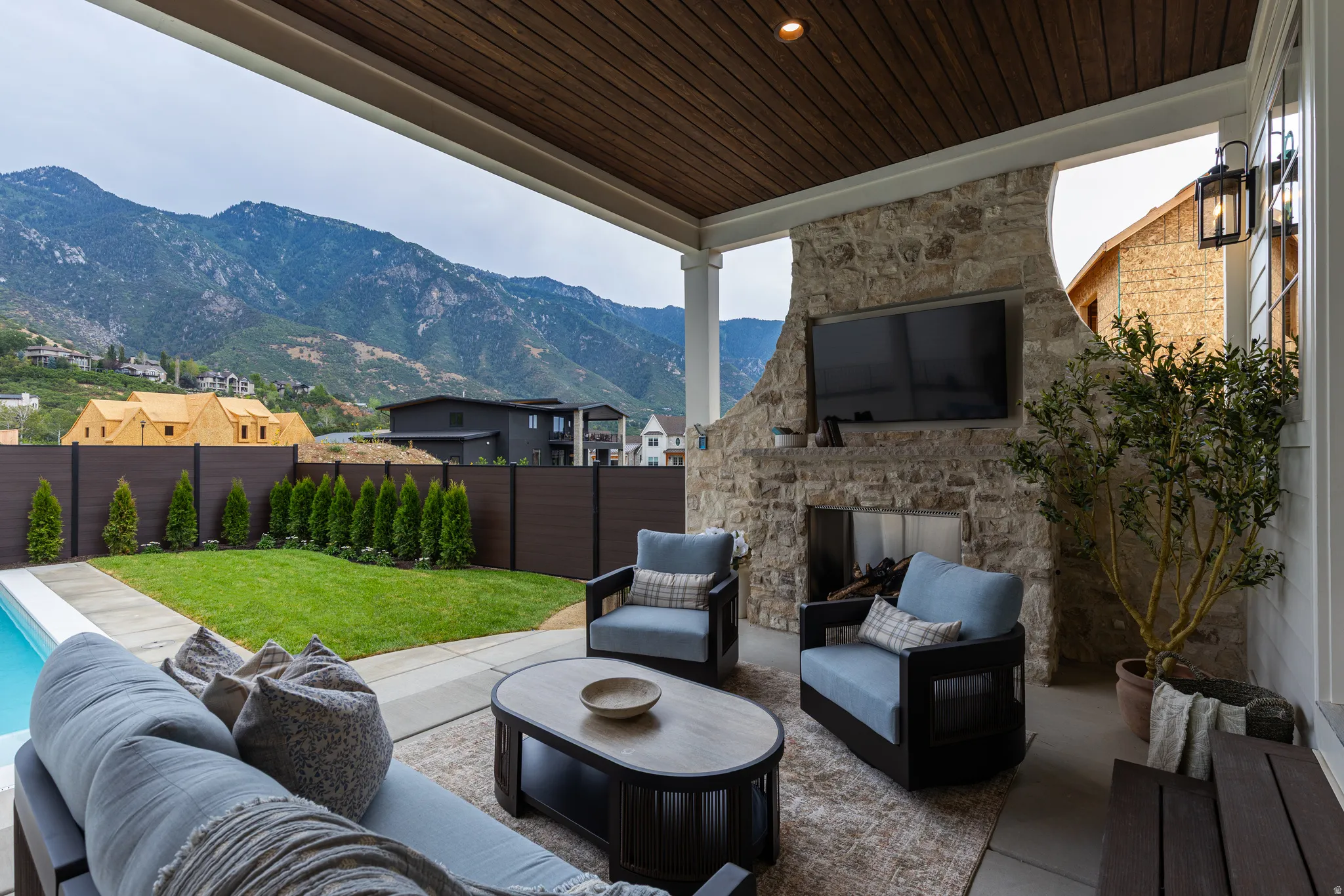 Covered outdoor patio featuring a stone fireplace, wood-finish ceiling, and mounted outdoor lighting