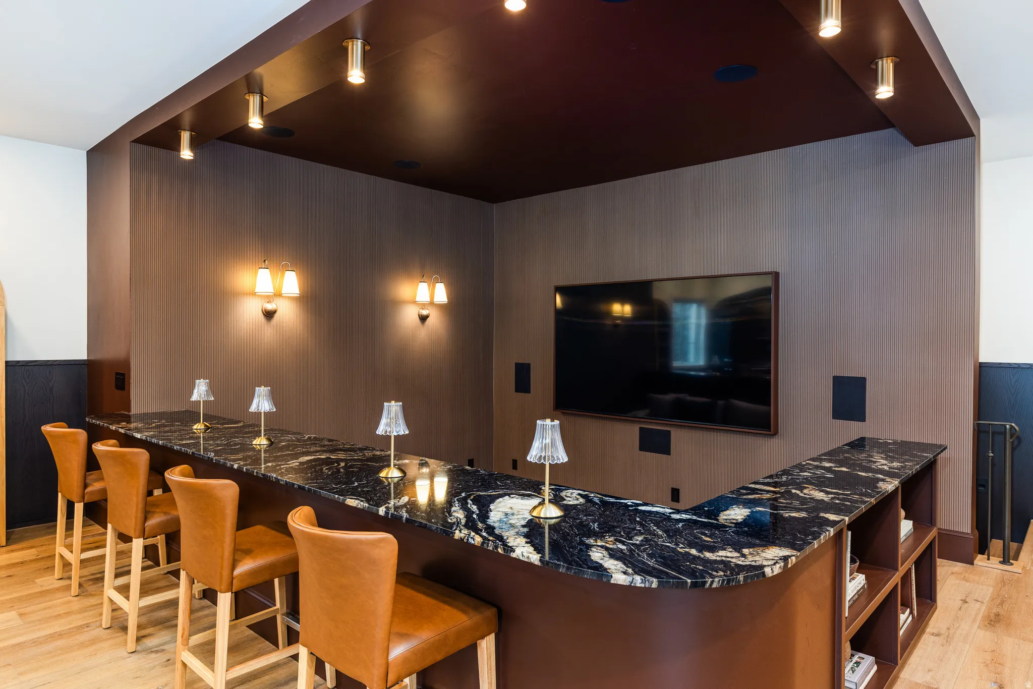Custom bar with a dark, patterned countertop, built-in shelving, and wood-finish flooring