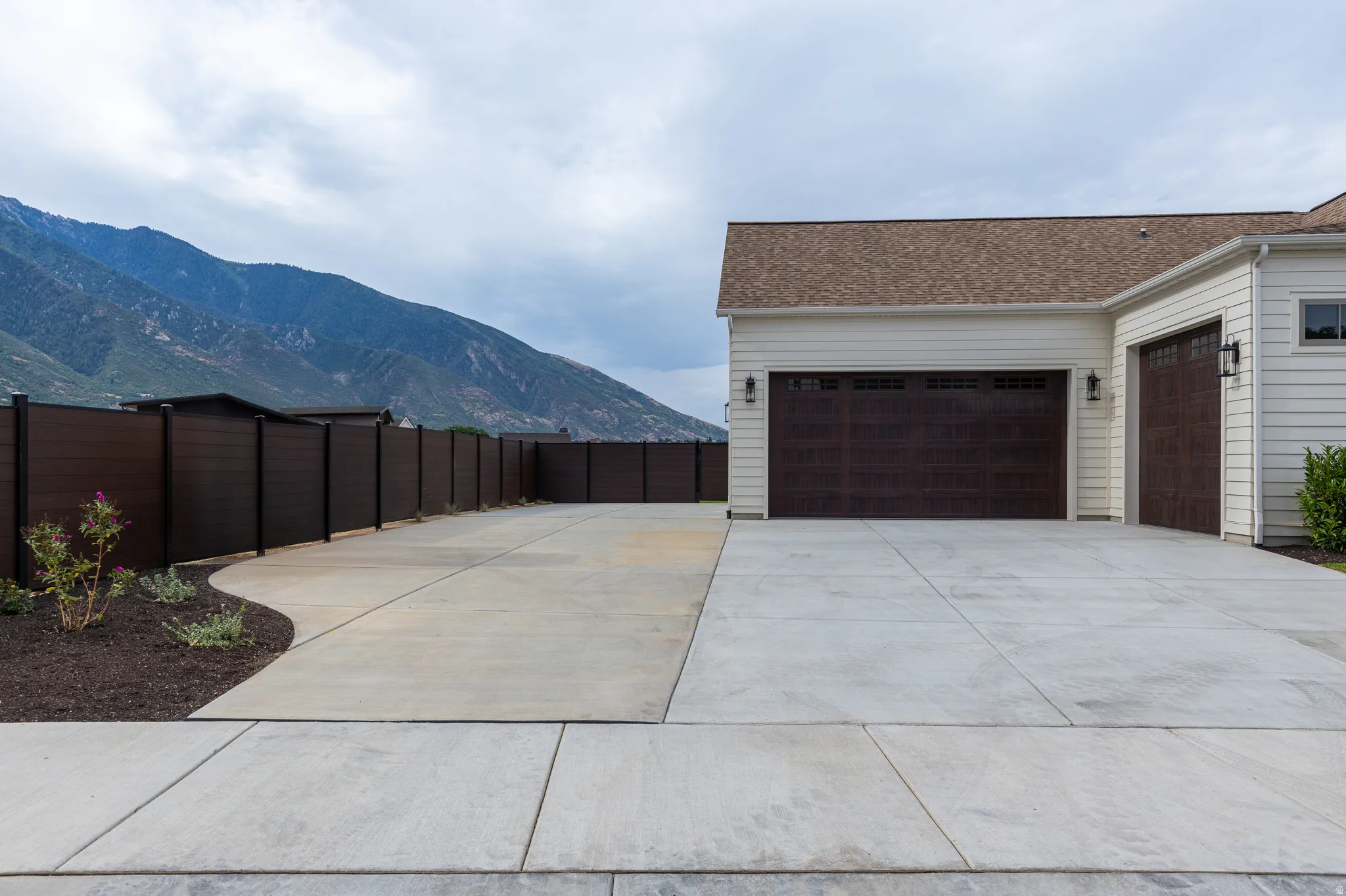 Attached multi-car garage with dark wood-finish doors and exterior sconce lighting