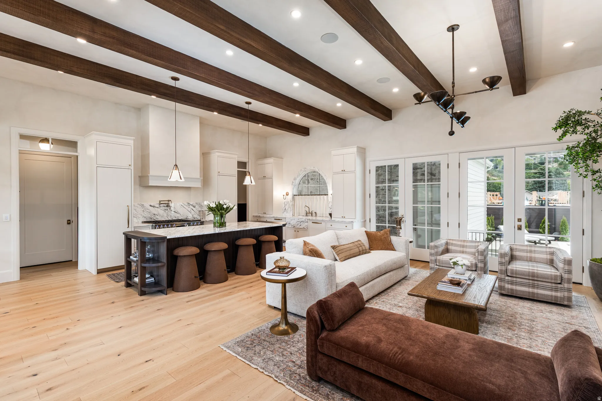 Open-concept living space with exposed ceiling beams, light wood-finish flooring, and white French doors