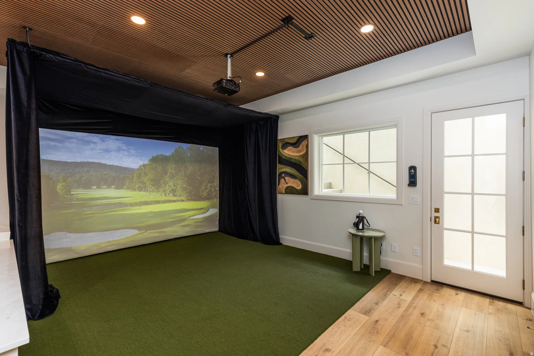 Dedicated golf simulator space featuring a large projection screen and artificial turf flooring