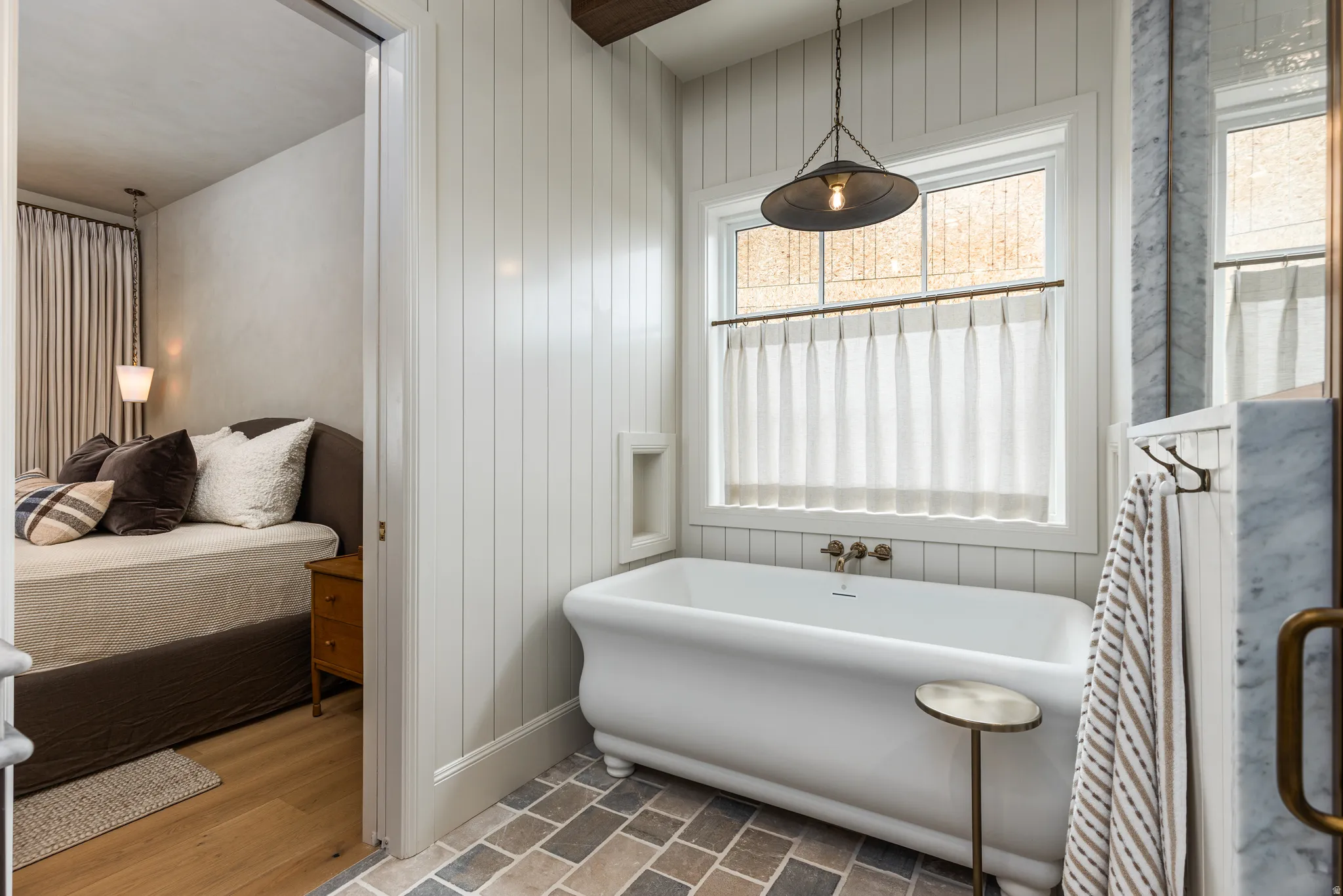 Bathroom featuring a freestanding clawfoot tub, vertical plank wall paneling, and a window with a hanging pendant light