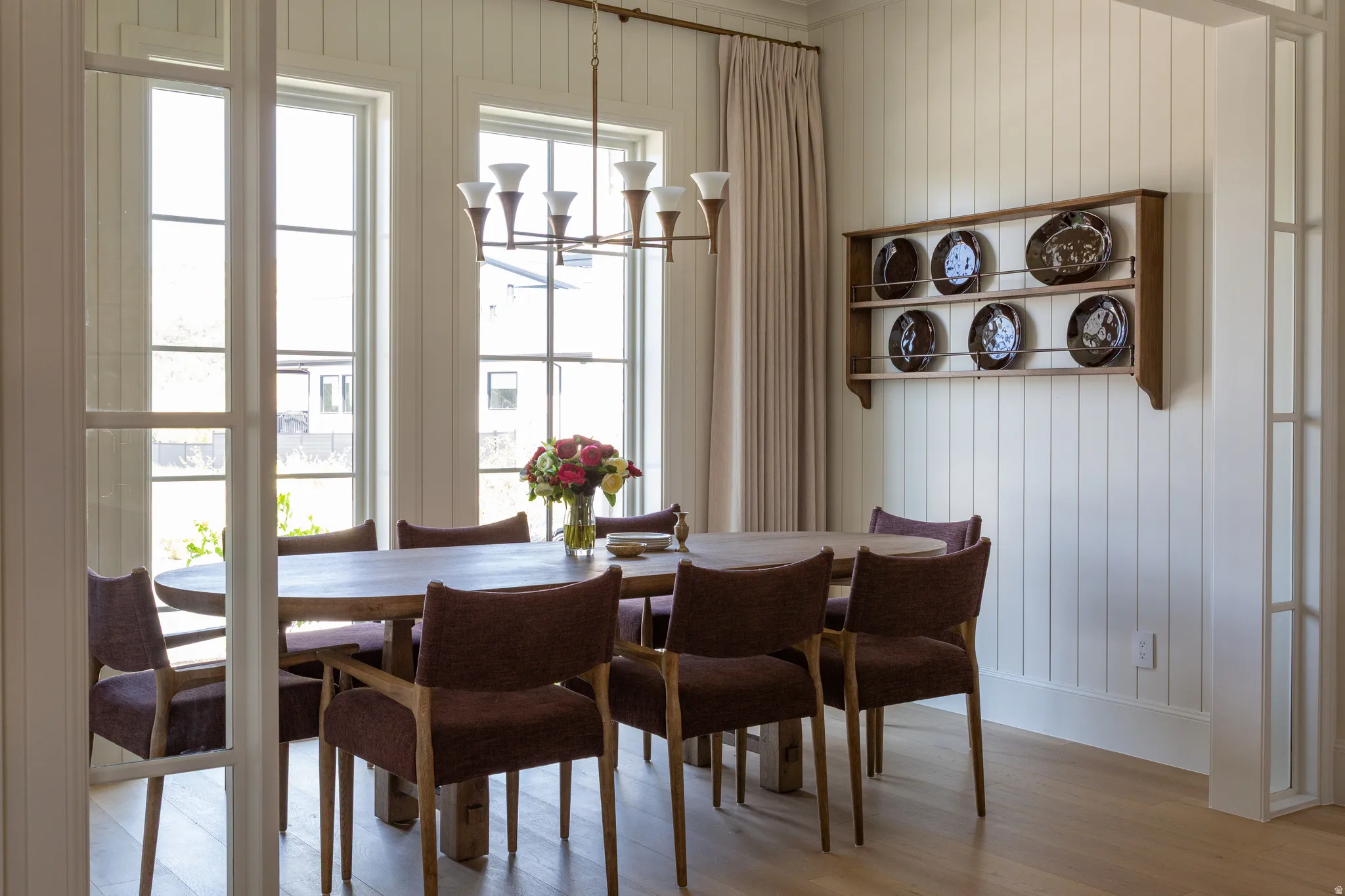 Vertical plank wall paneling with a built-in display shelf, wood-finish flooring, a multi-pane glass door, and expansive windows