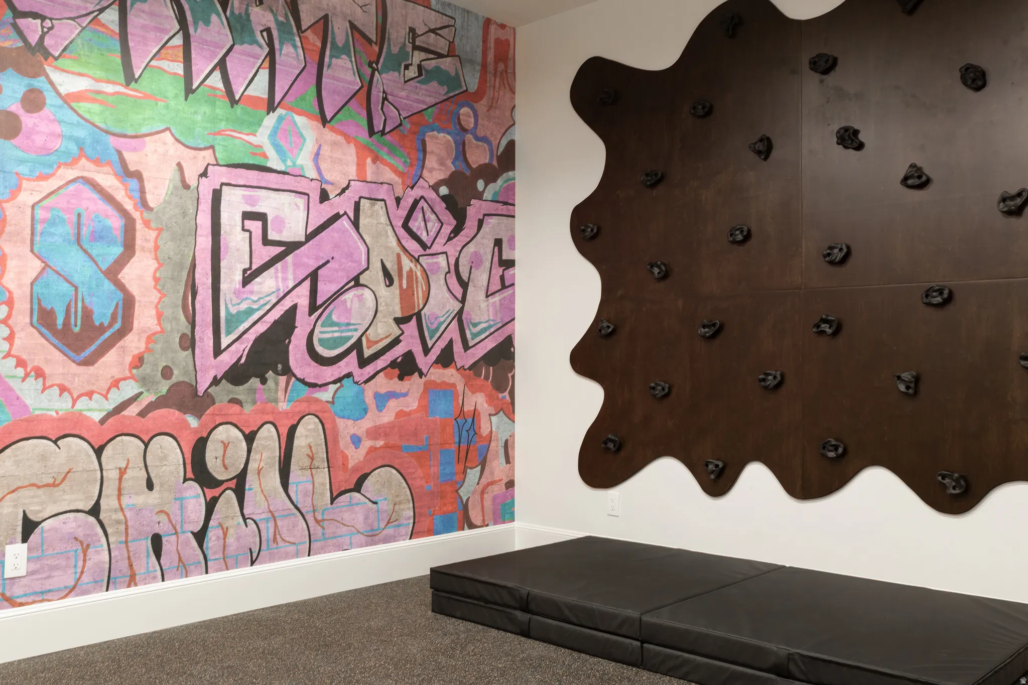 Textured wall covering with graphic art, built-in climbing wall with varied holds, and carpeted flooring