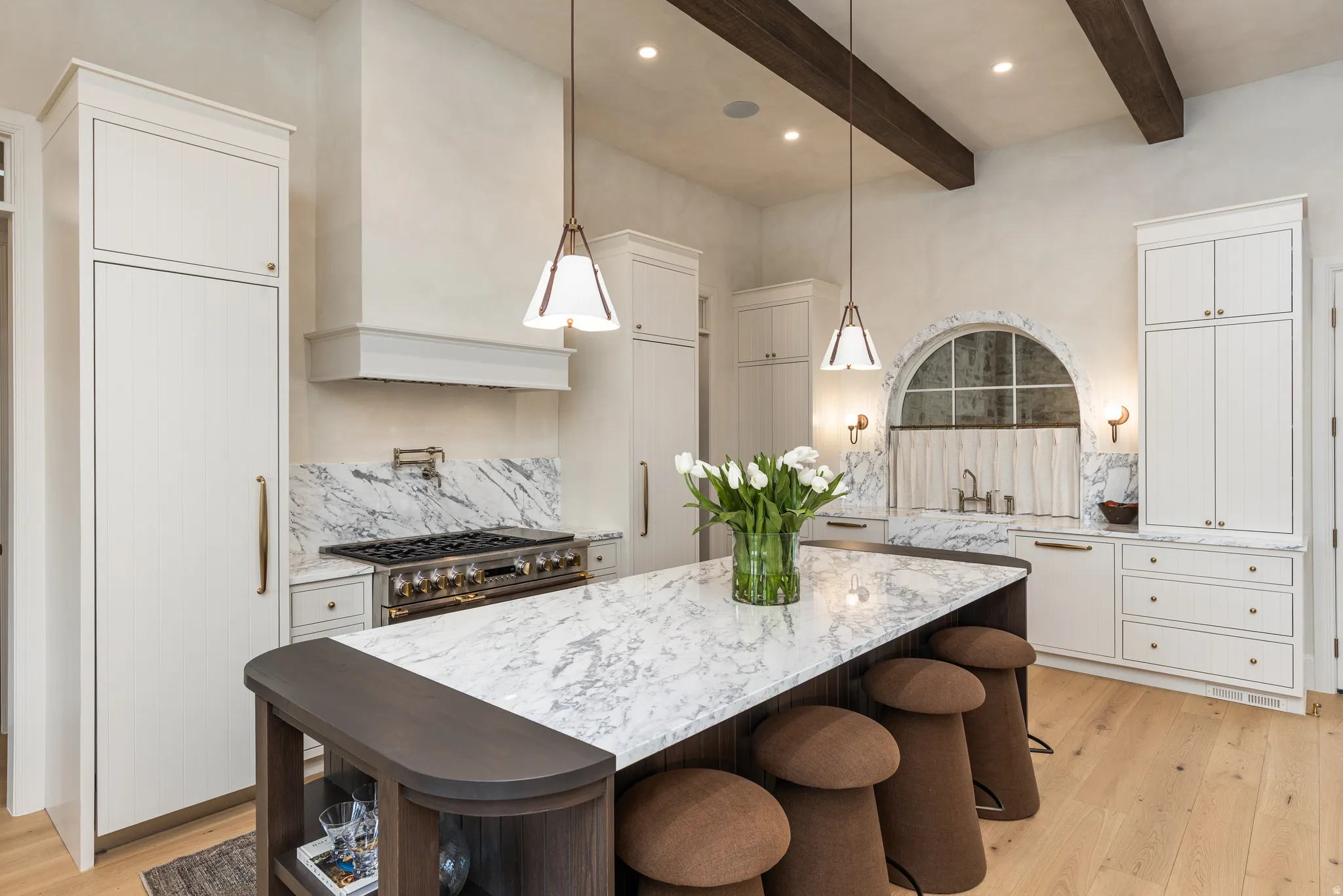 Gourmet kitchen with a large central island, professional-grade range, custom cabinetry, marble countertops, and exposed ceiling beams