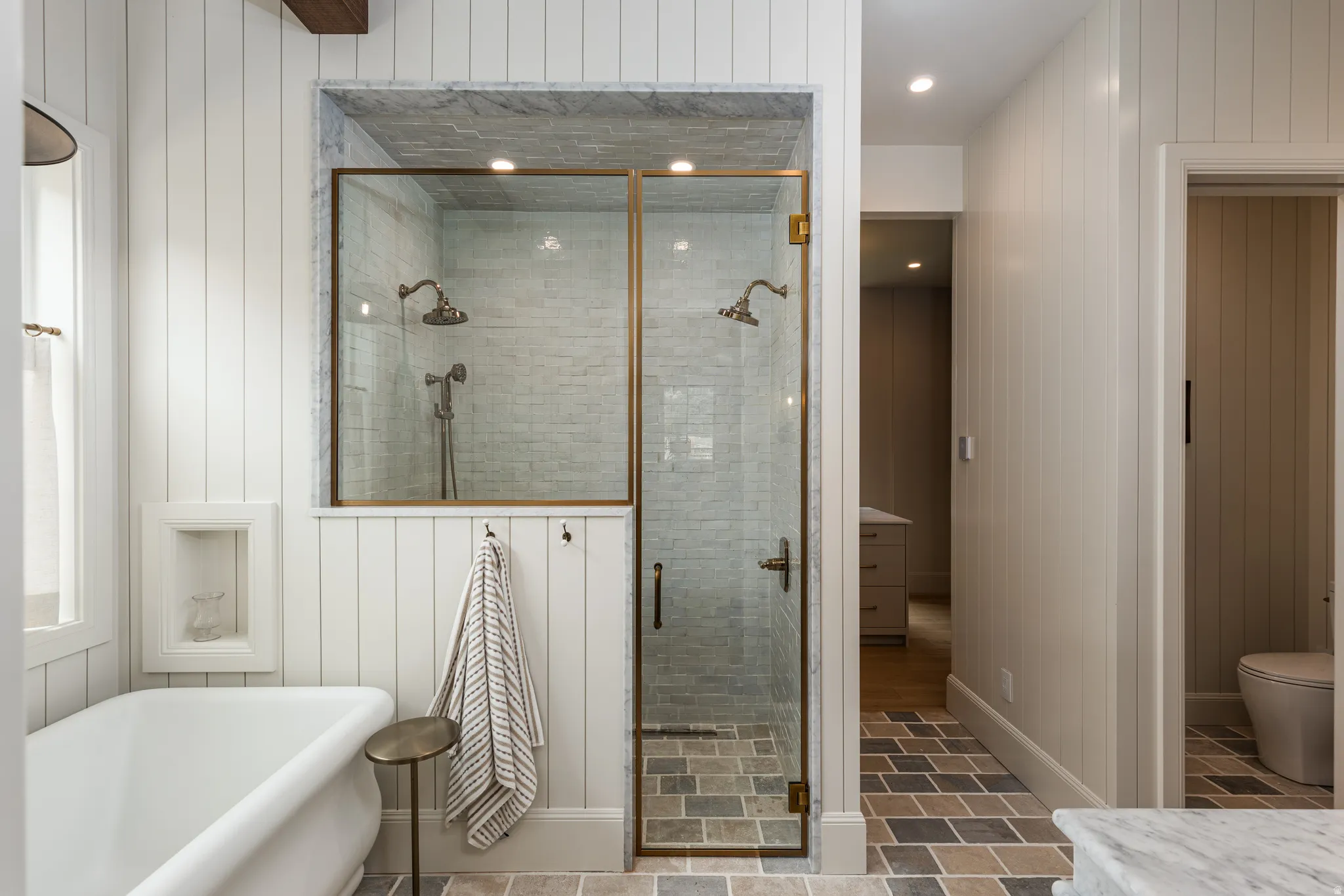 Spacious shower enclosure with dual bronze-finish showerheads and light-toned subway tile surround