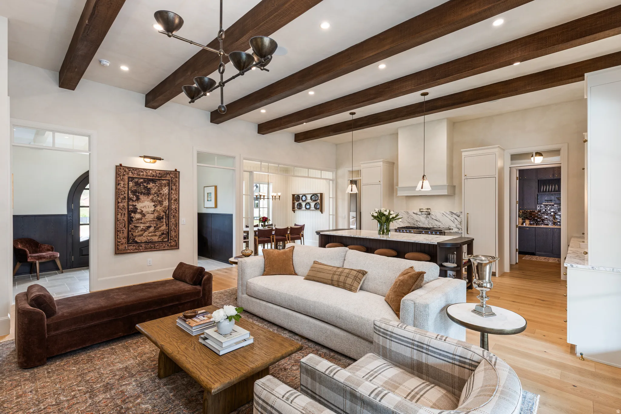 Open-concept living area featuring exposed wood beams, recessed lighting, and light wood-finish flooring