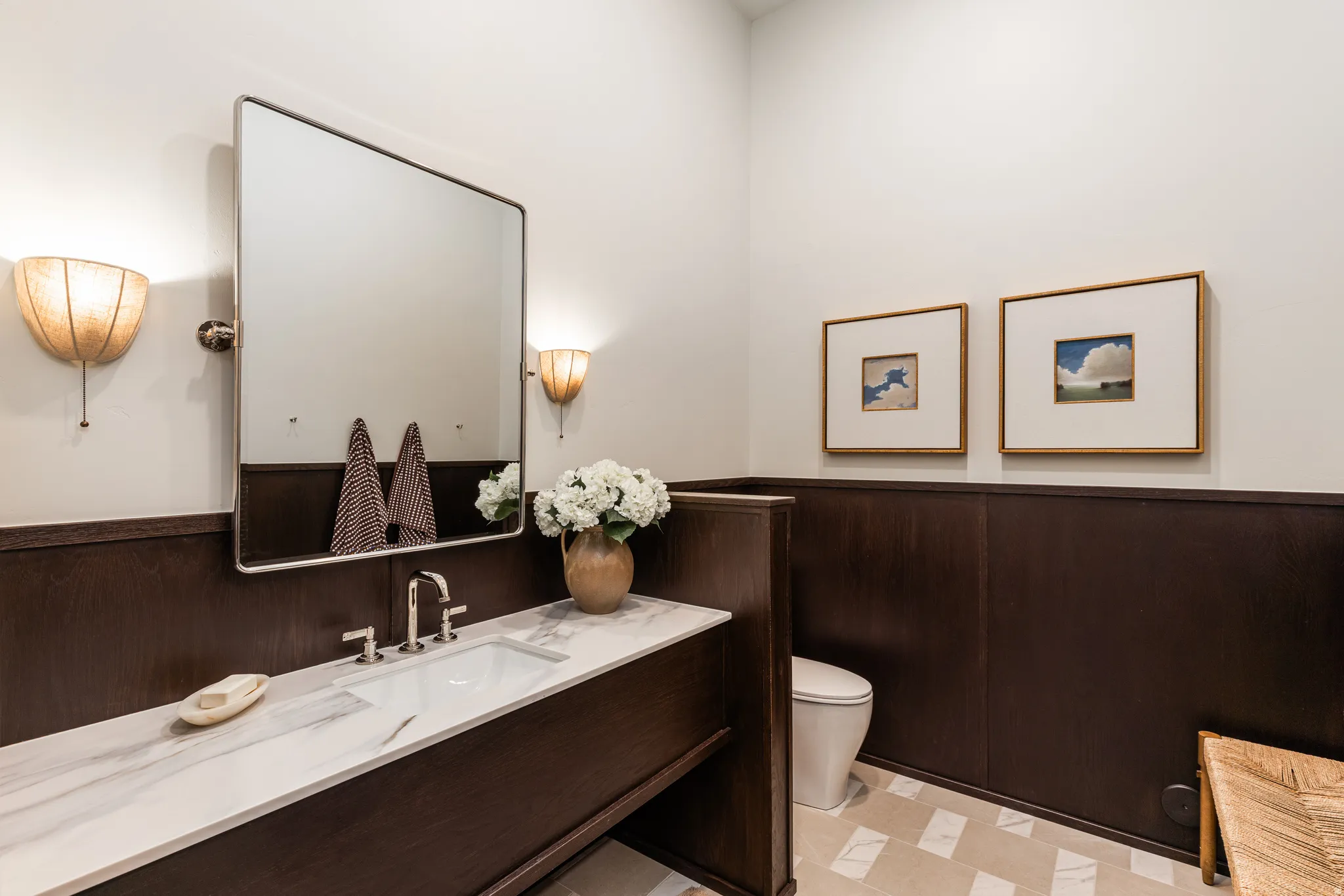 Vanity with a white countertop and integrated sink, framed by wood-finish wainscoting and wall-mounted sconces