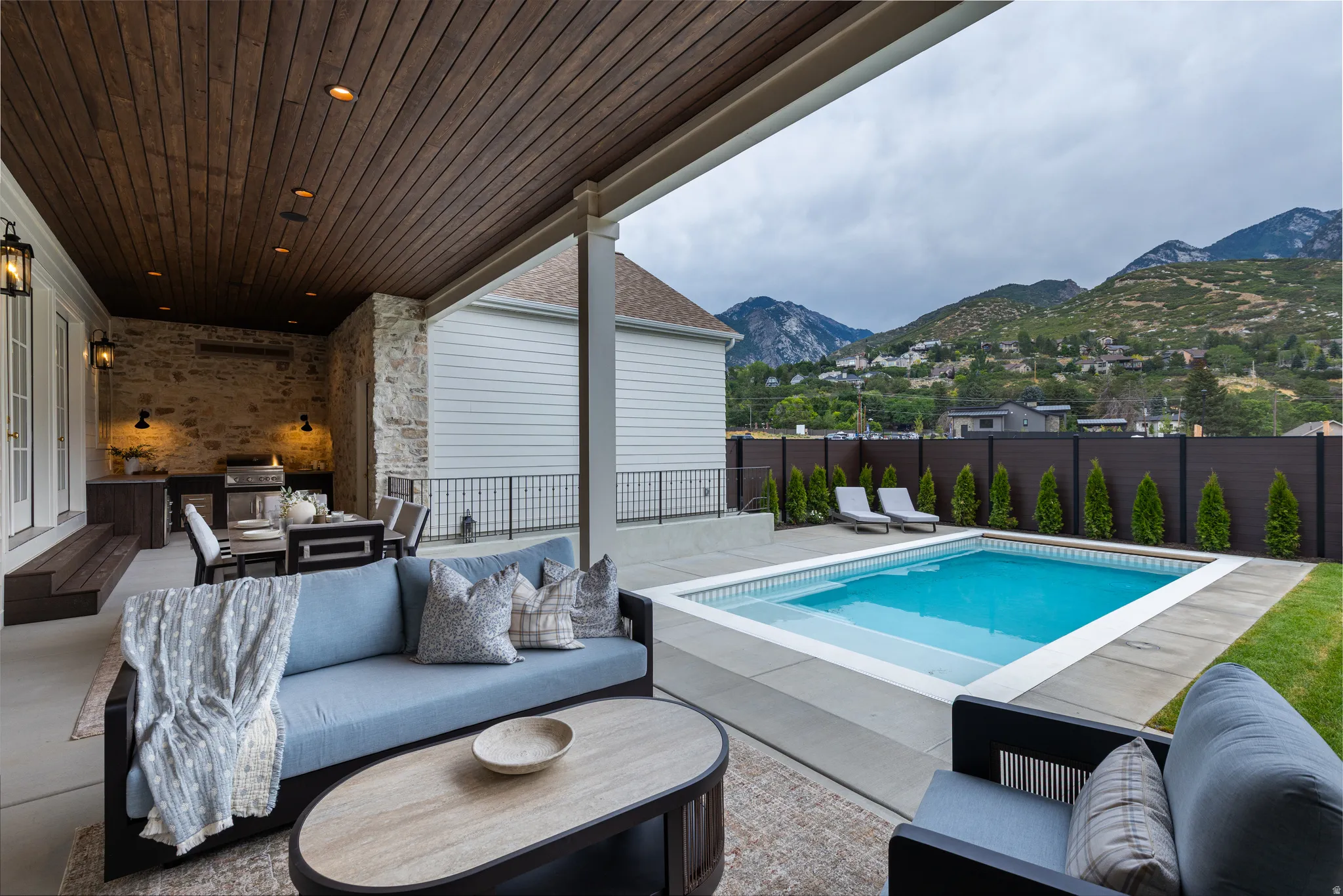 Covered patio with a wood-plank ceiling, stone accent wall, and built-in outdoor kitchen
