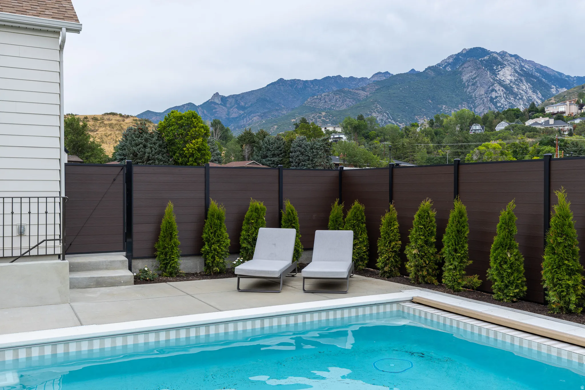 Outdoor pool with concrete decking, a privacy fence, and mountain scenery