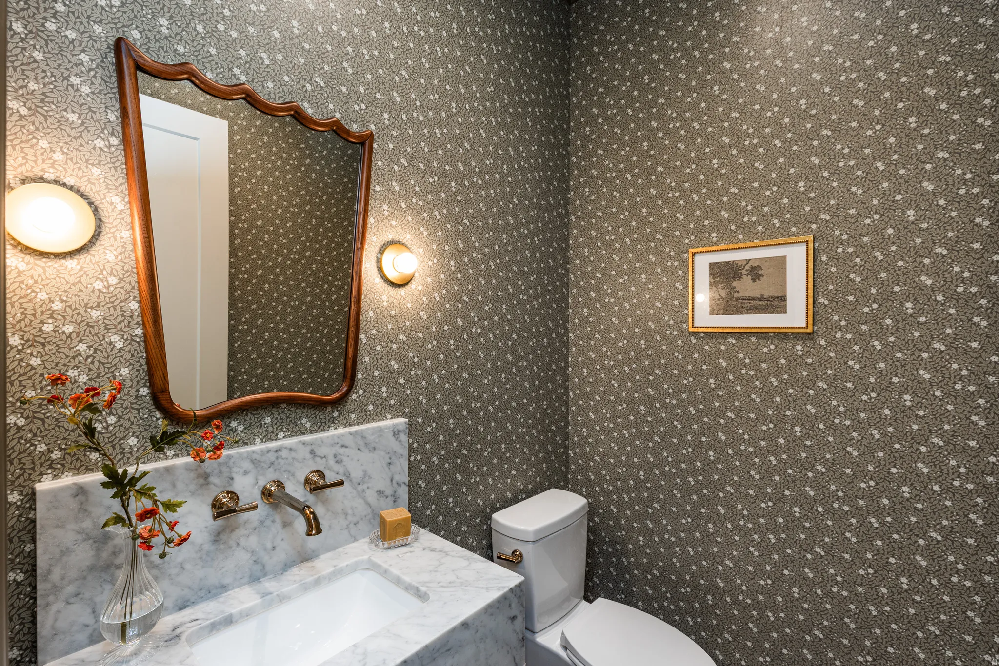 Elegant powder room featuring a marble-topped vanity with polished chrome fixtures, an ornately framed mirror with curved detailing, and dual wall-mounted sconces