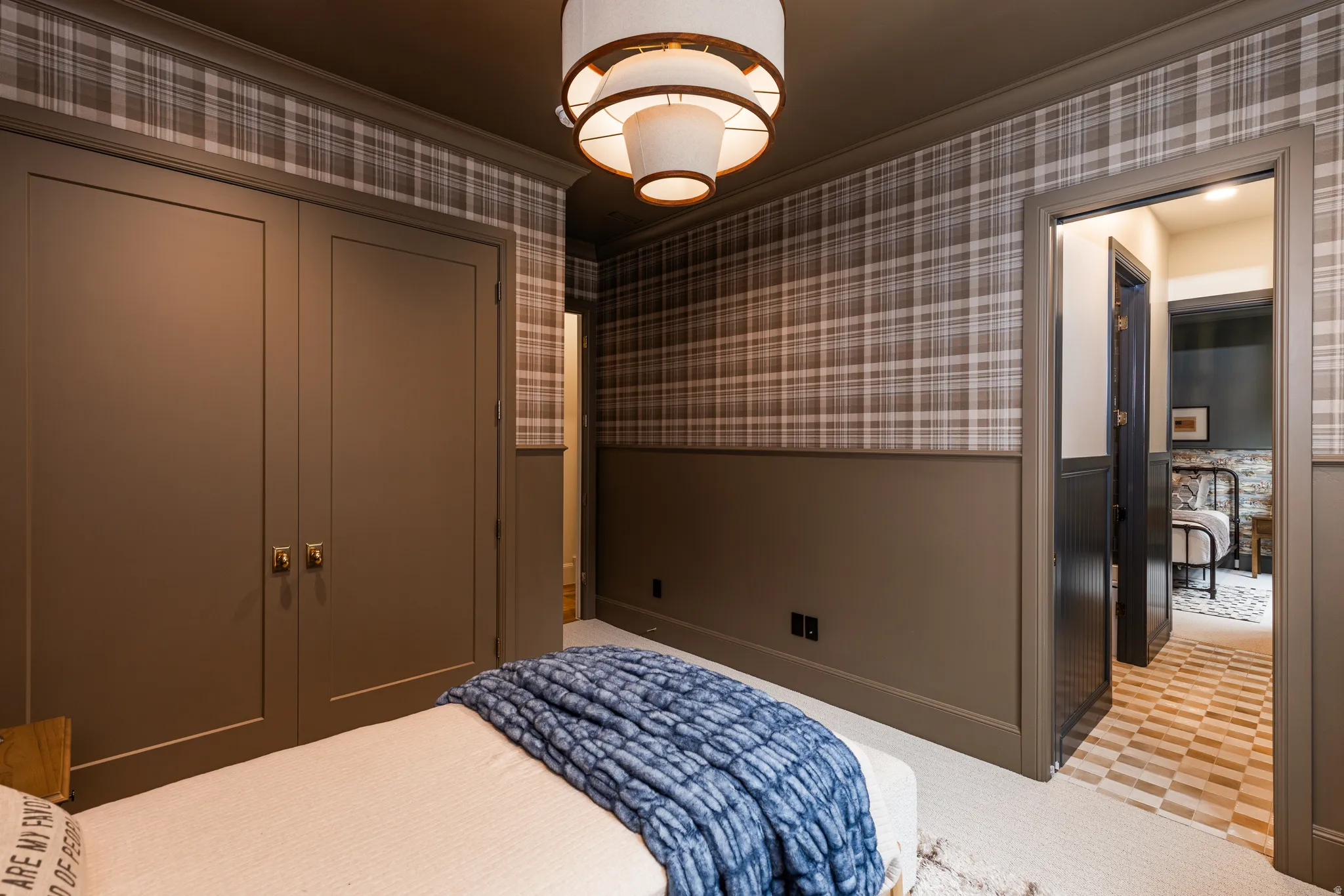 Room featuring plaid wallpaper, dark wainscoting, and a layered ceiling fixture