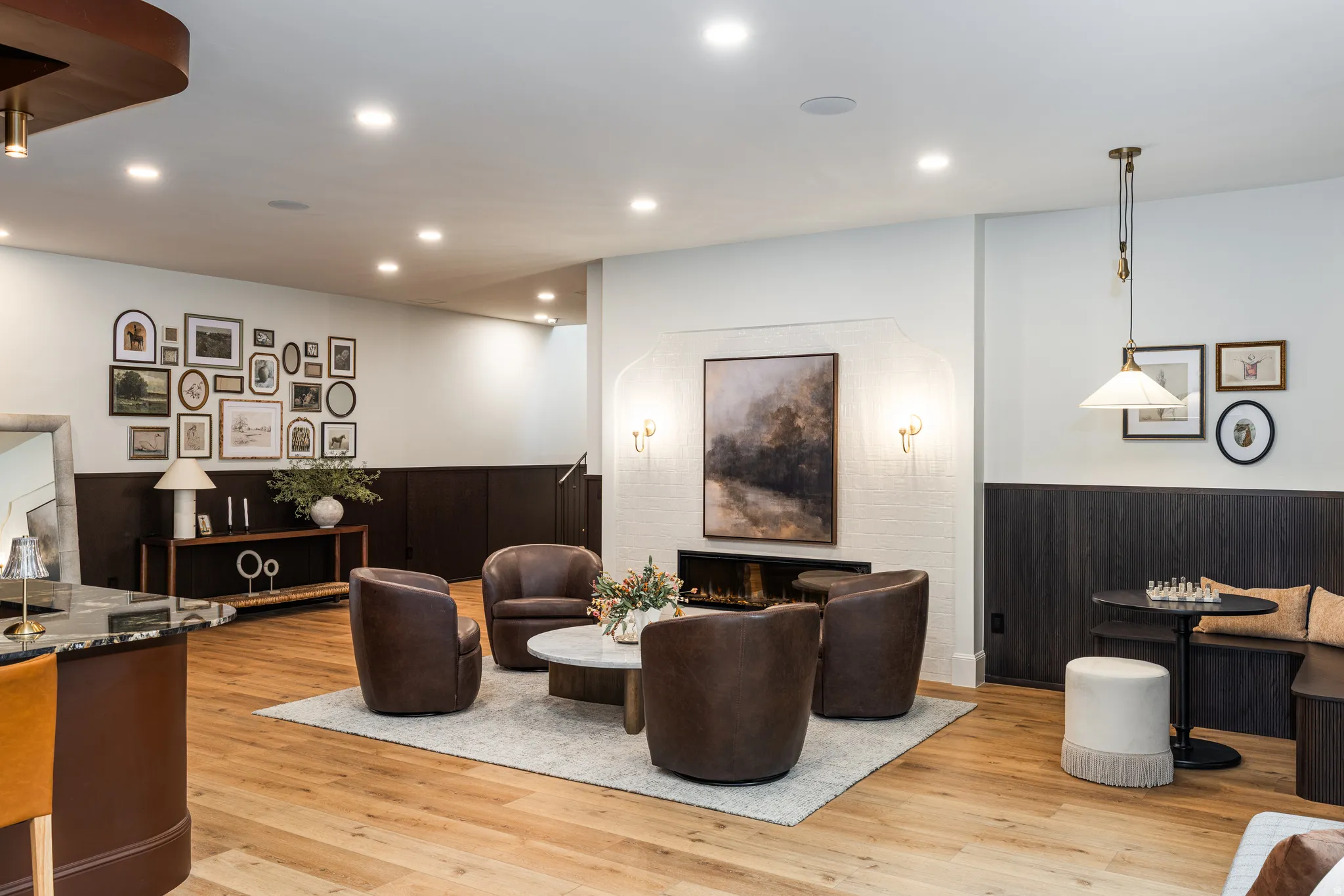 Spacious recreation area featuring light wood-finish flooring, recessed lighting, and a linear electric fireplace with sconce lighting