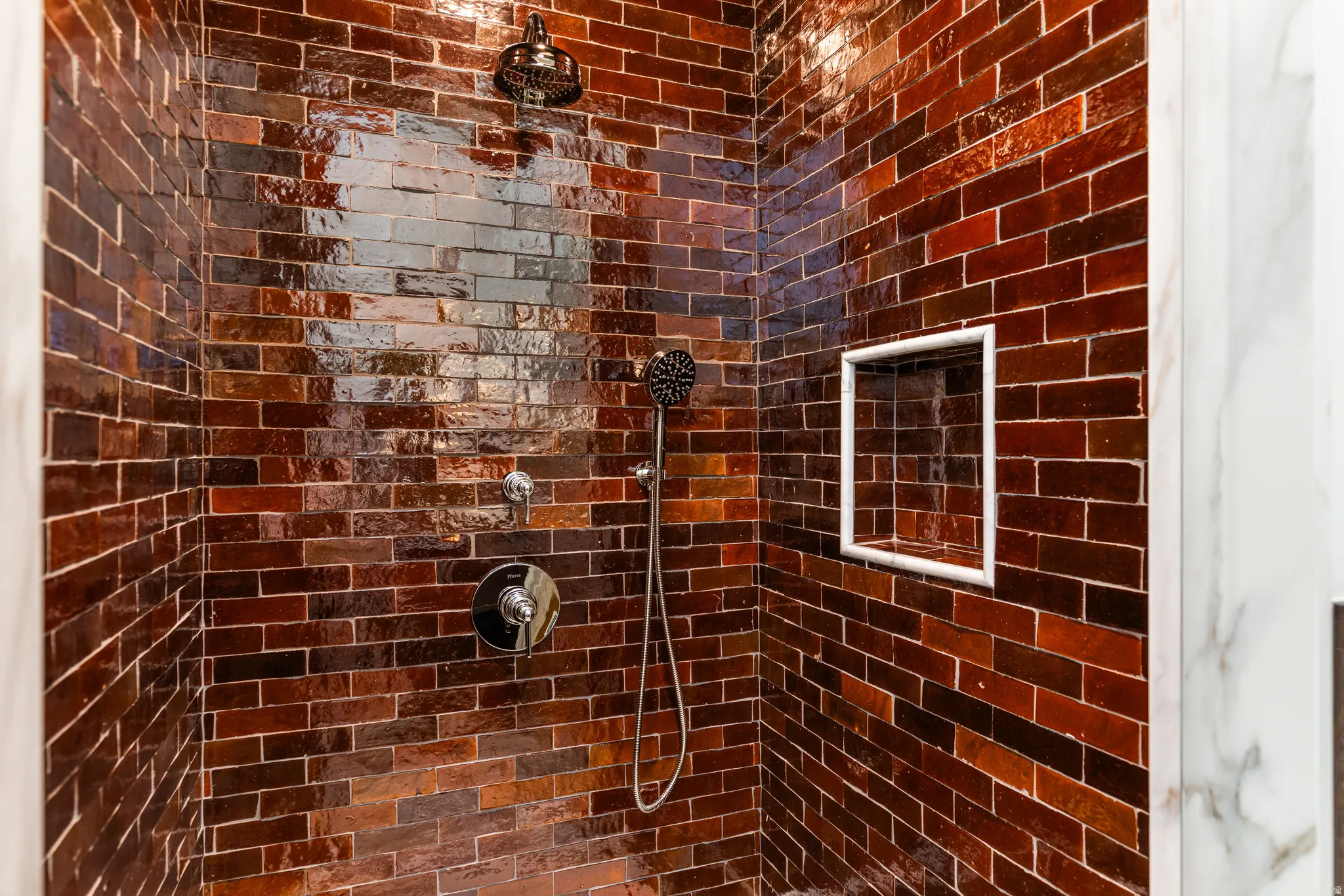Shower with brick-patterned tile, rain shower head, handheld spray, polished chrome fixtures, and an integrated shower niche