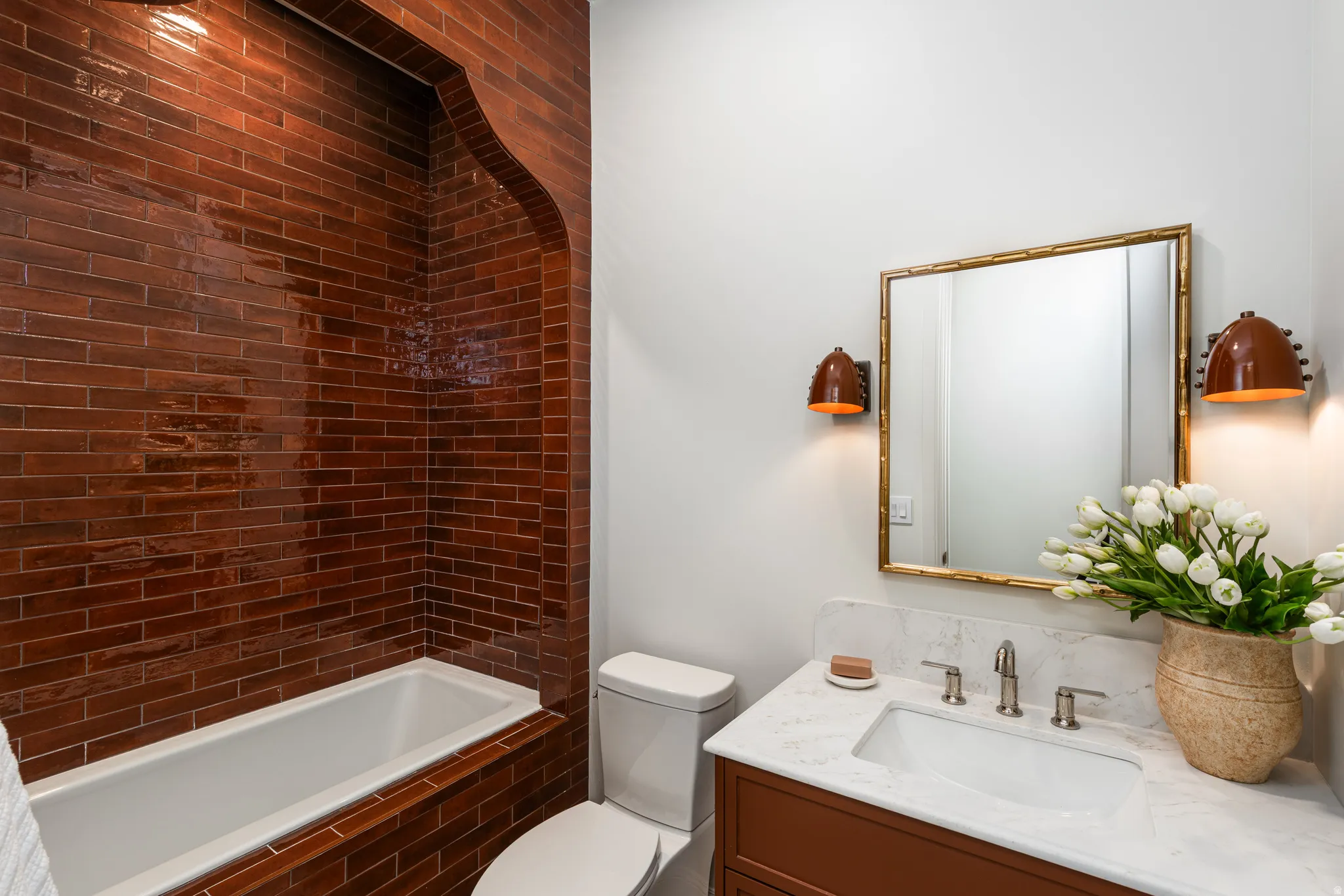 Bathroom featuring a subway-tiled tub surround with an arched alcove, a white built-in tub, and a white toilet