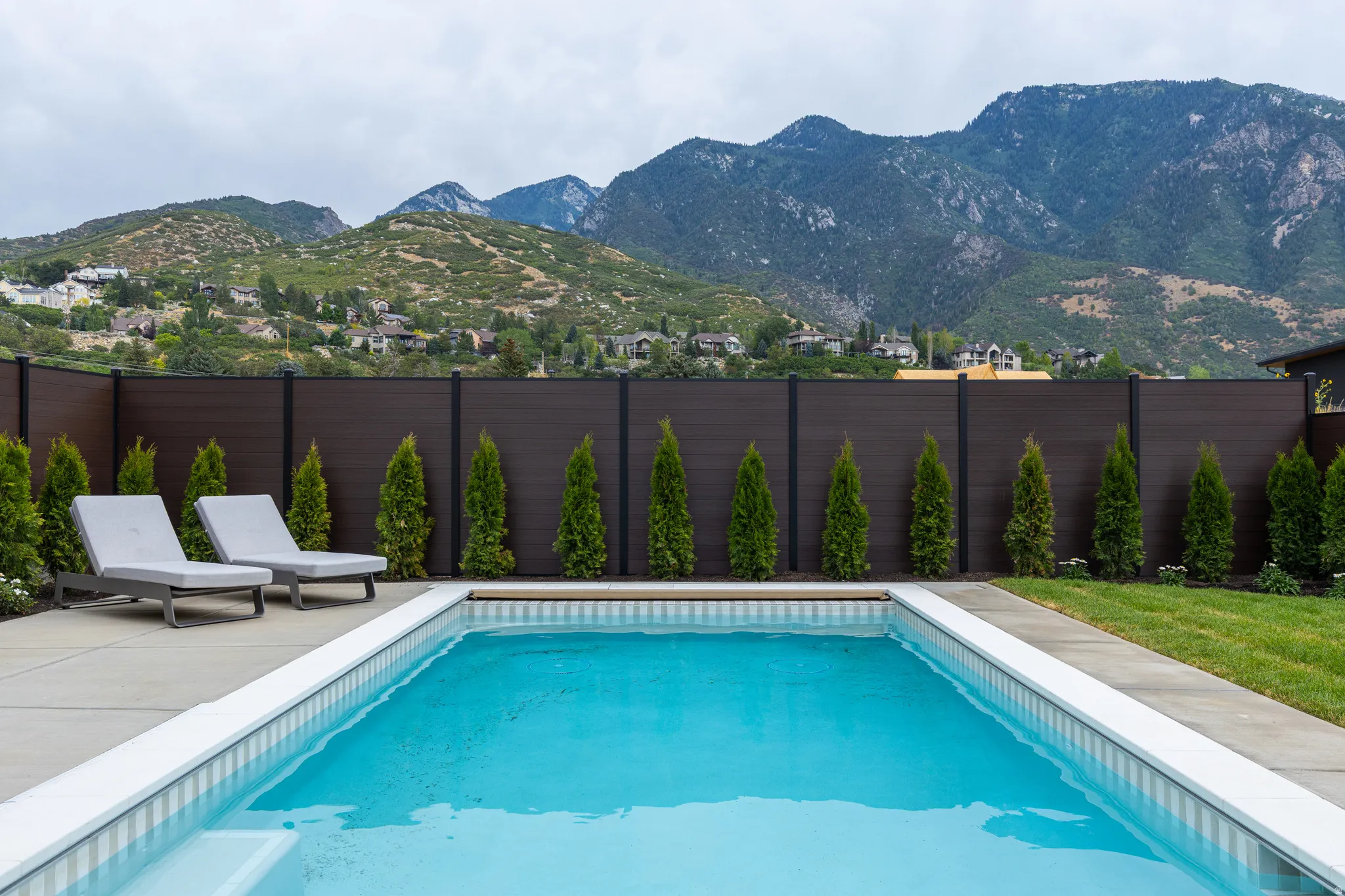 In-ground swimming pool with surrounding concrete decking, bordered by a manicured lawn and a privacy fence