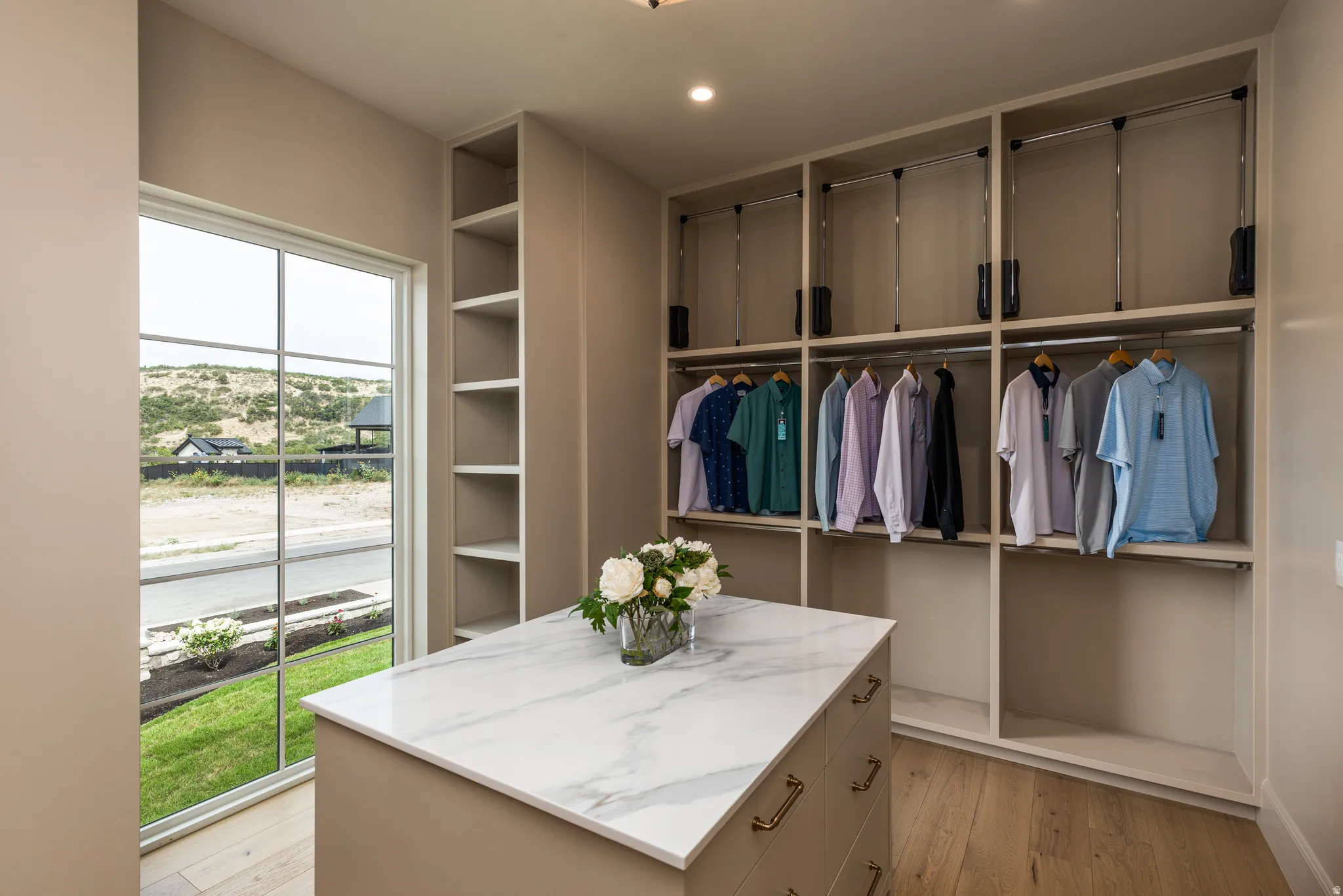 Spacious custom closet featuring extensive built-in shelving, integrated hanging rods, and a central island with a stone-finish countertop and brass-finish hardware