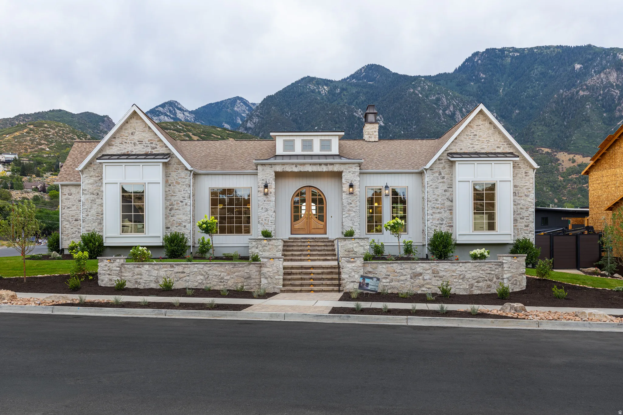 Stone and board-and-batten exterior with an arched wood entry door, multiple gables, and large windows