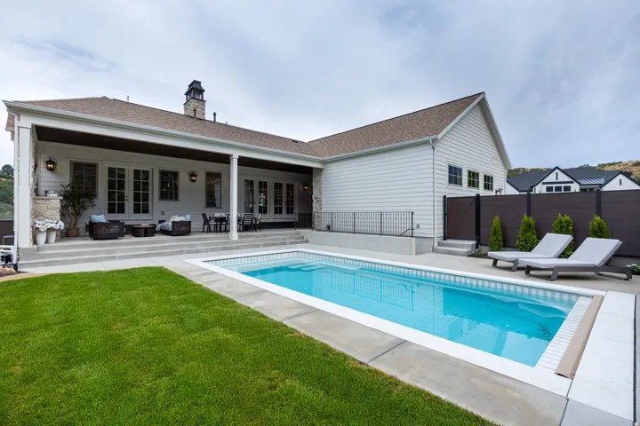 Rear exterior with a rectangular swimming pool, concrete surround, and grassy area