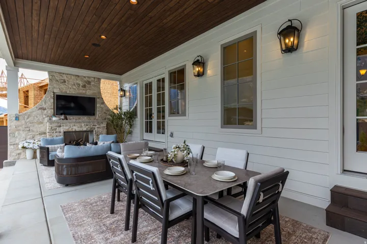 Covered outdoor patio featuring a wood-panel ceiling with recessed lighting, a stone-clad fireplace, and white horizontal siding