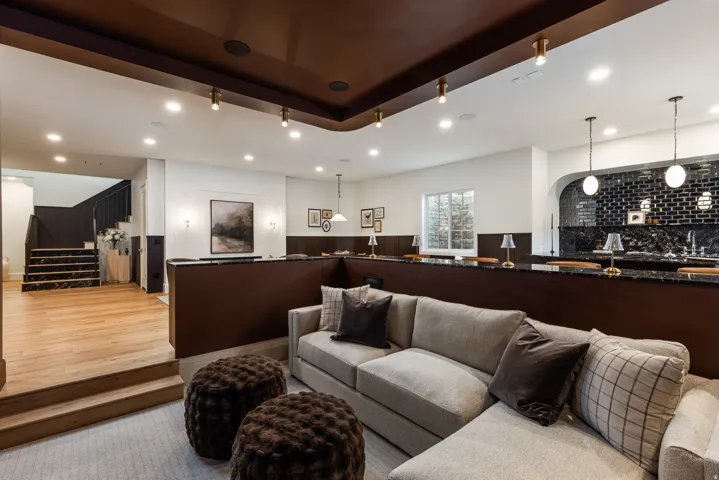 Multi-level entertainment space featuring a dedicated wet bar with black subway tile, a recessed archway, and dual pendant lighting