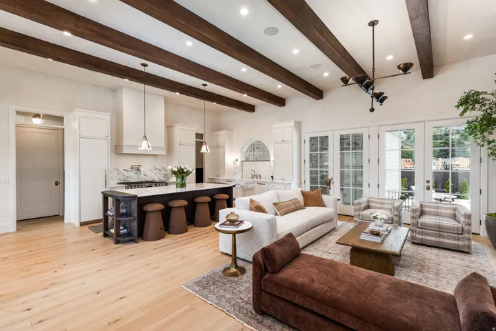 Open-concept living space with exposed ceiling beams, light wood-finish flooring, and white French doors