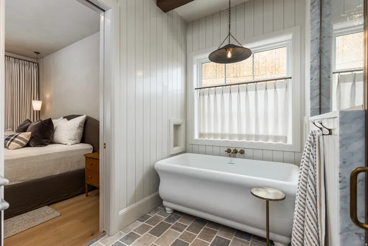 Bathroom featuring a freestanding clawfoot tub, vertical plank wall paneling, and a window with a hanging pendant light