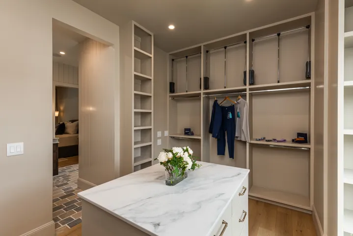 Custom closet featuring a large stone-finish island with drawers and chrome hardware