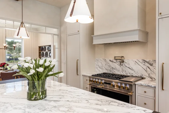 Gourmet kitchen featuring a professional-grade gas range with a pot filler, a custom range hood, and extensive stone countertops with matching backsplash