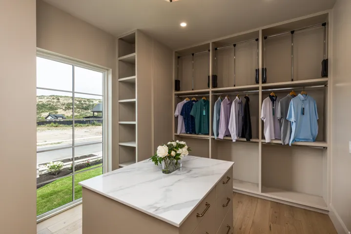 Spacious custom closet featuring extensive built-in shelving, integrated hanging rods, and a central island with a stone-finish countertop and brass-finish hardware