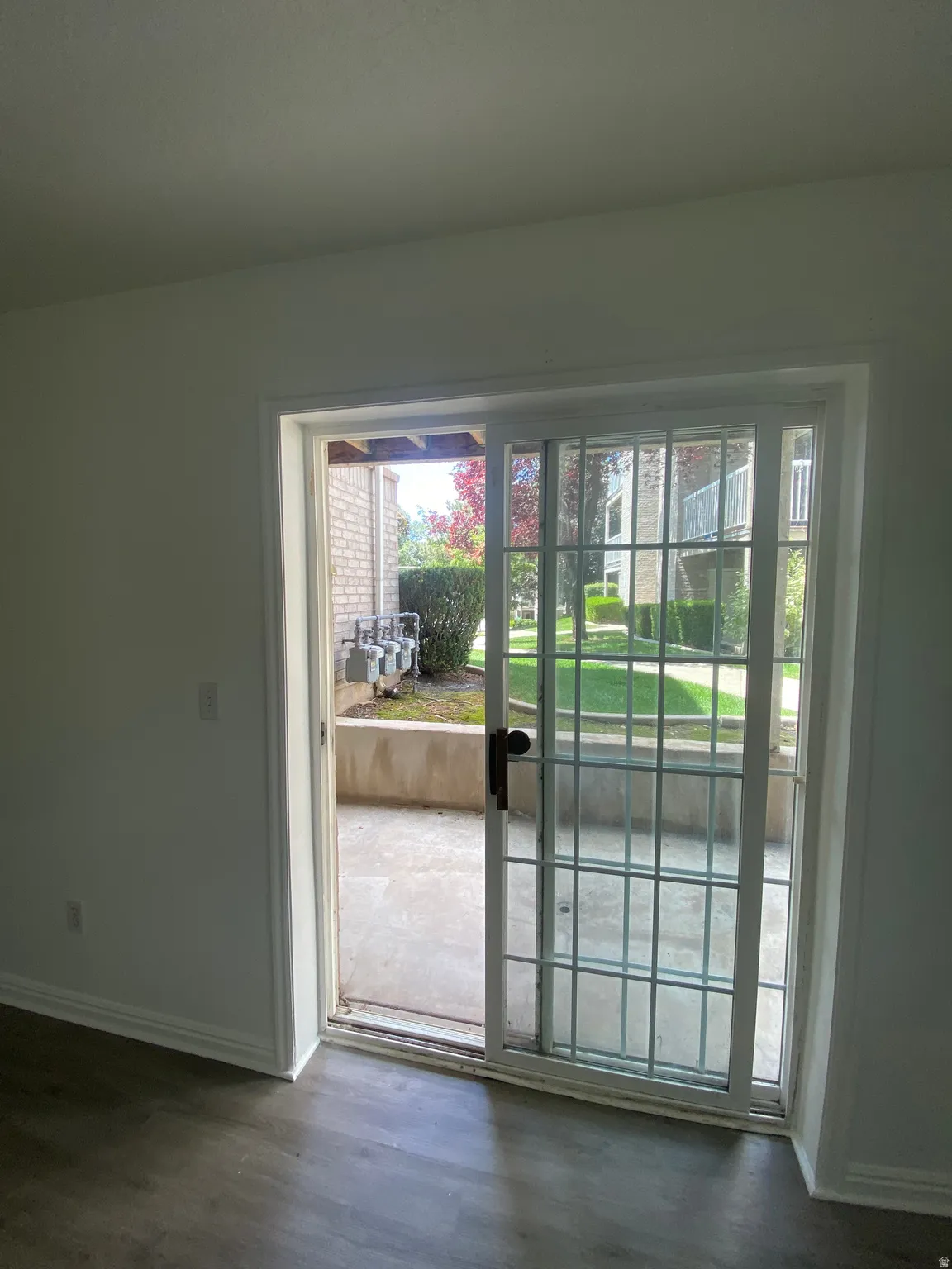 Sliding glass door opening to a private patio space with concrete flooring and a partial grid overlay
