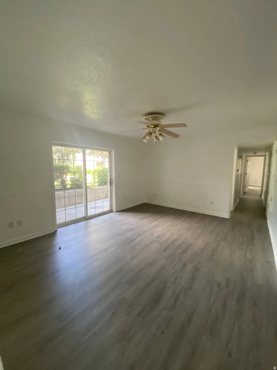 Spacious living area featuring wood-finish flooring, a ceiling fan with integrated lighting, and a sliding glass door leading to an outdoor patio