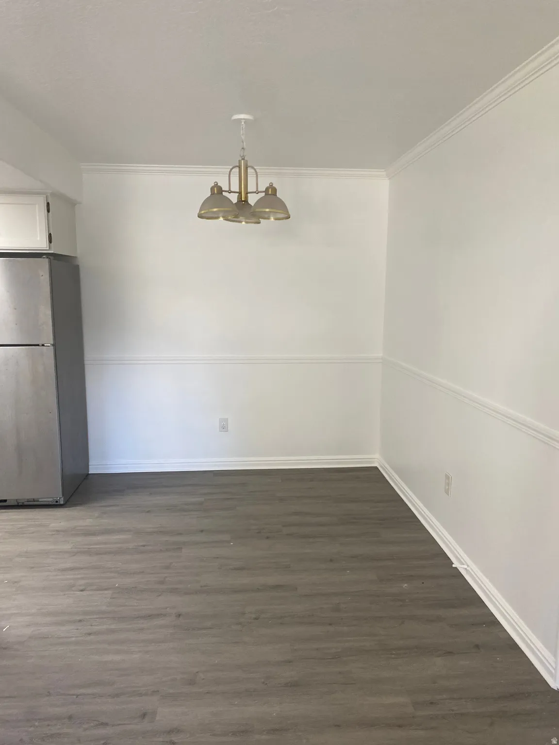 Dining area featuring a three-light chandelier with frosted glass shades, crown molding, chair rail molding, and wood-finish flooring