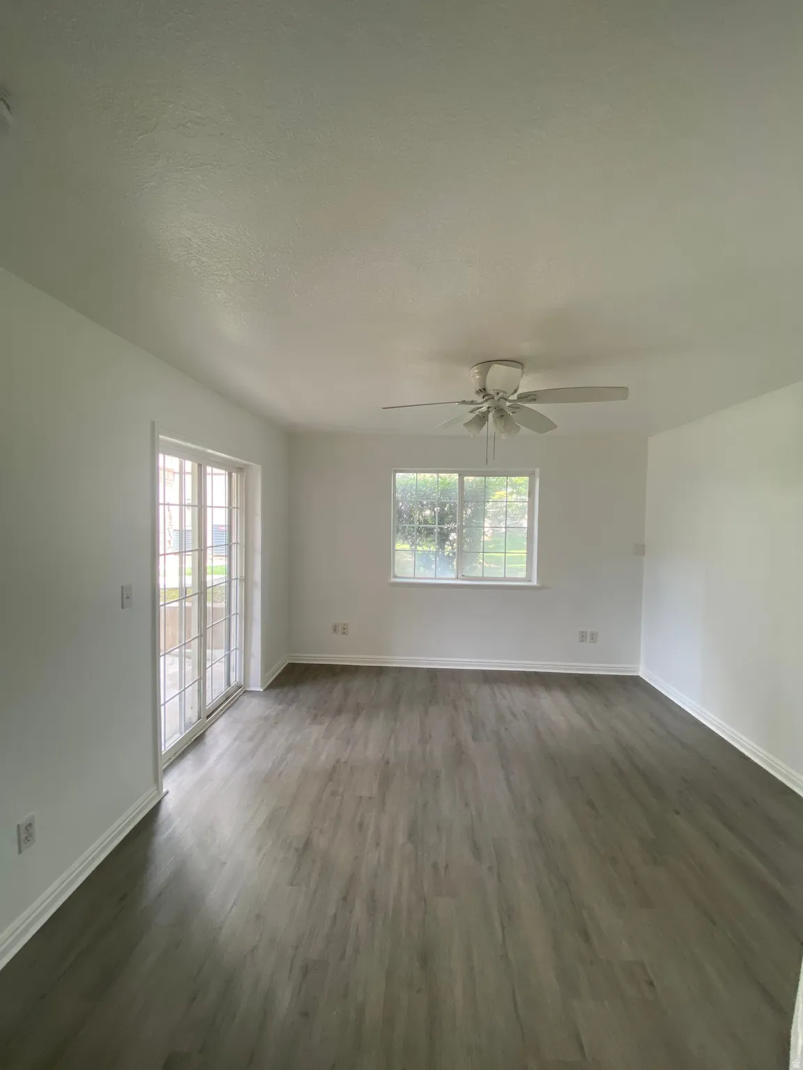 Spacious room featuring wood-finish flooring, white baseboards, and a ceiling fan