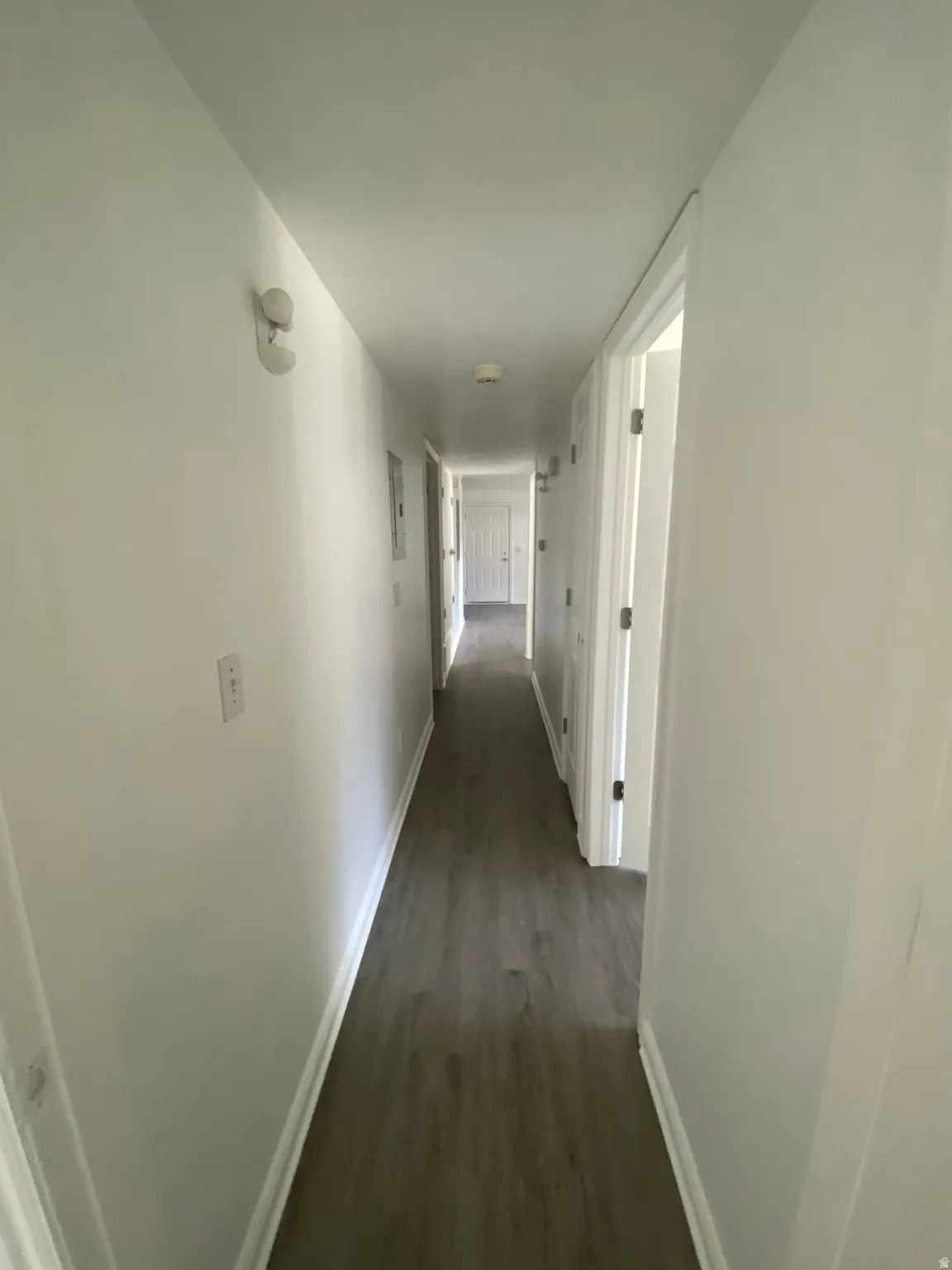 Long hallway featuring wood-finish flooring, white walls, and white trim