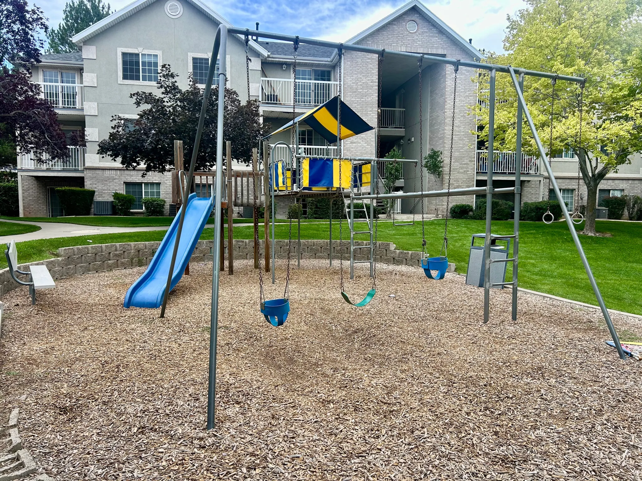 Community playground featuring a slide, multiple swings, monkey bars, and wood chip surfacing