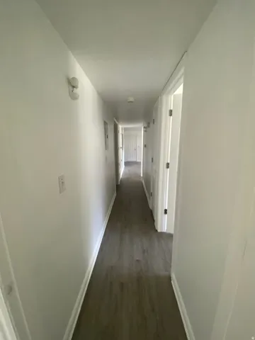 Long hallway featuring wood-finish flooring, white walls, and white trim