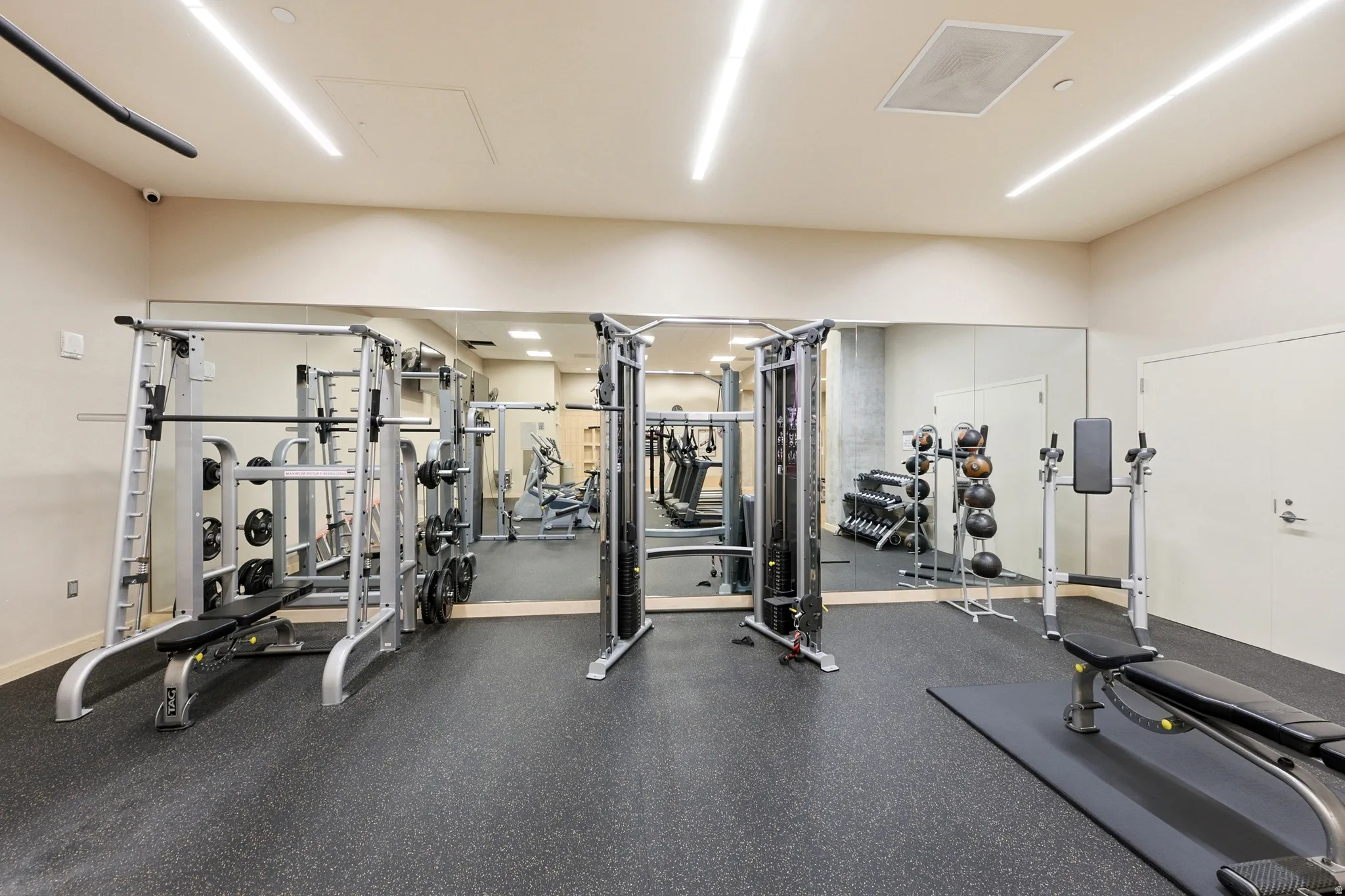Fitness room featuring extensive mirrored walls, rubberized flooring, linear ceiling lighting, and two white panel doors