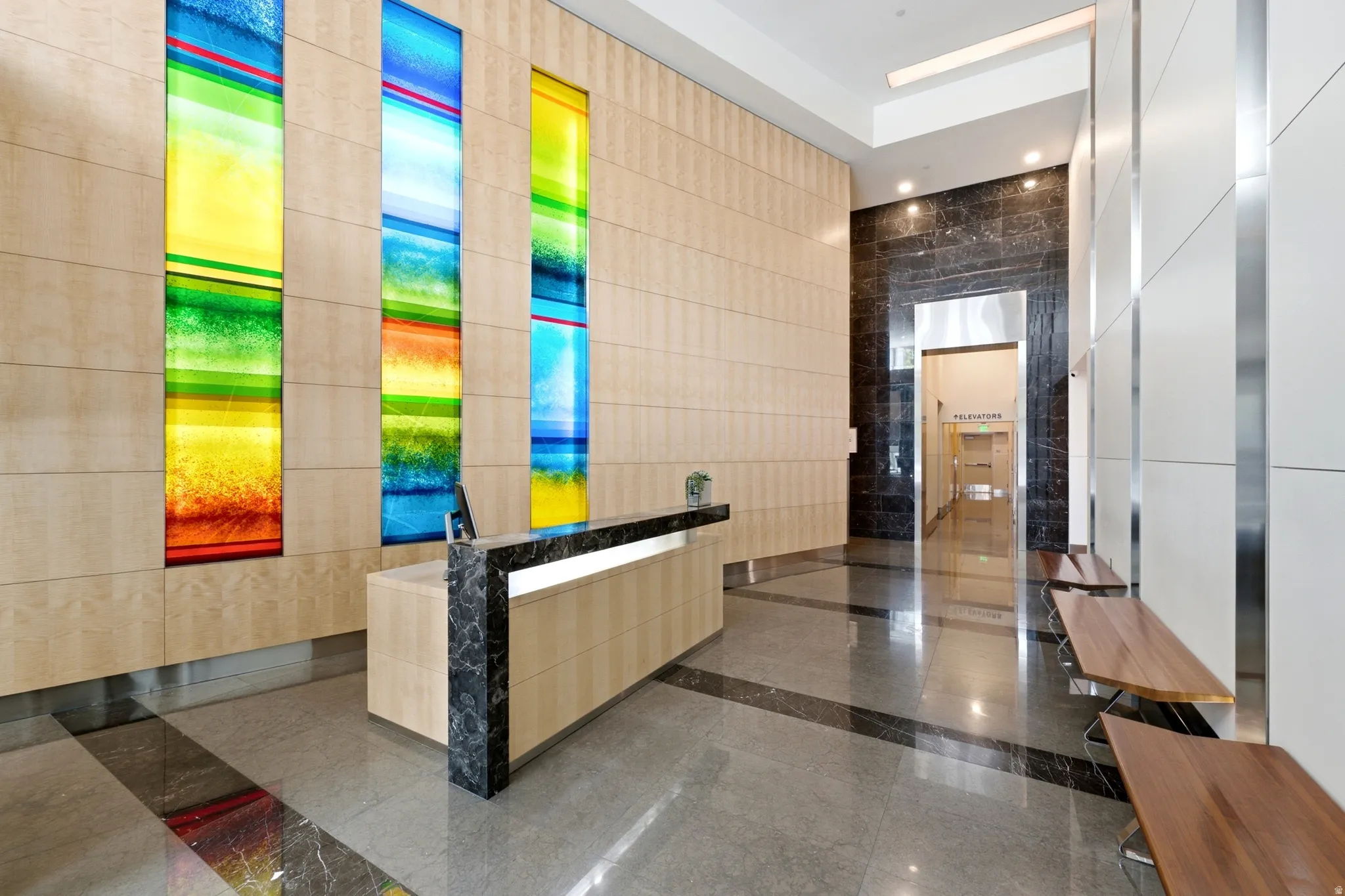 Lobby featuring a reception desk, wood-paneled walls, colorful vertical light panels, polished stone flooring, and built-in wood benches