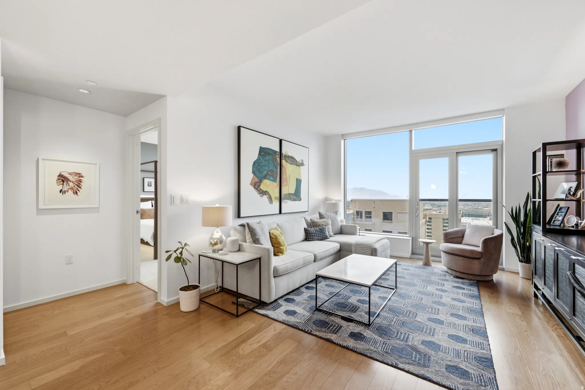 Open-concept living area featuring wood-finish flooring, recessed lighting, and expansive floor-to-ceiling windows with balcony access