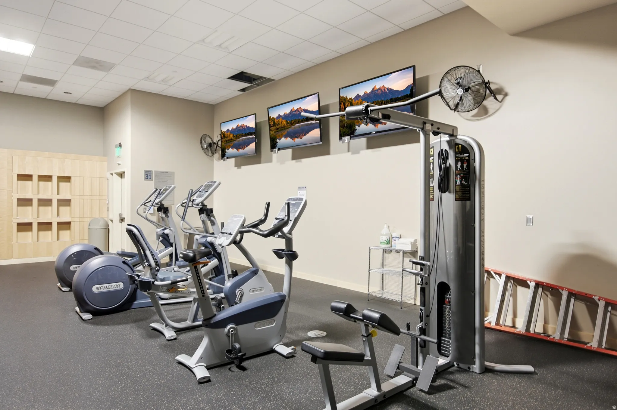 Fitness center featuring rubberized flooring, multiple cardio machines, a weight machine, and wall-mounted televisions