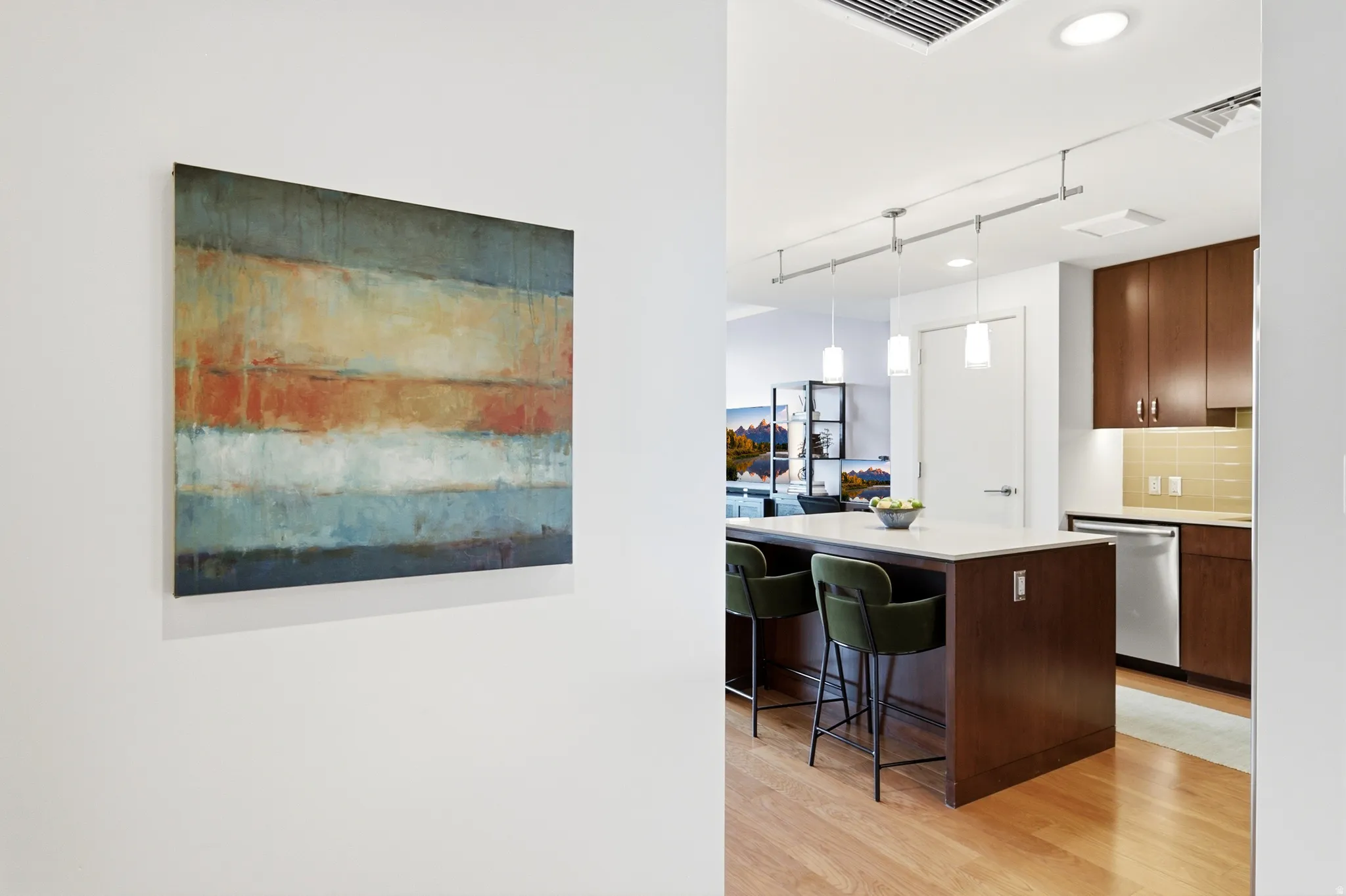 Open-concept kitchen featuring wood-finish flooring, a central island with a light-toned countertop, dark wood cabinetry, and a stainless steel dishwasher